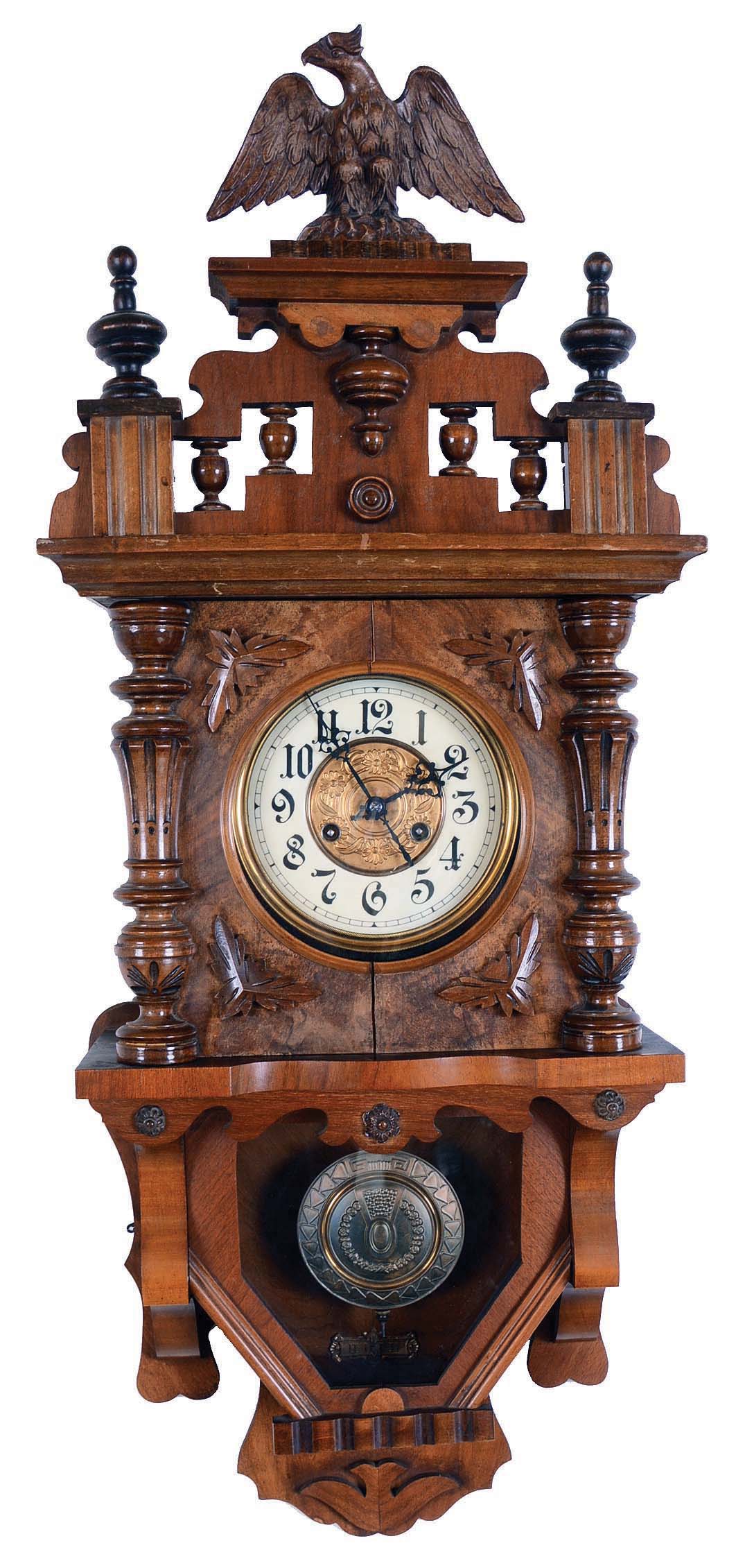 Junghans, Wurttemberg, Germany, "Freischwinger" type wall clock, 8 days, time and strike, spring driven movement in an Alt Deustch walnut case with glazed window over pressed brass pendulum and surmounted by eagle. The dial is a cream enamel two part with brass pressed center. — Antique Clocks Price Guide