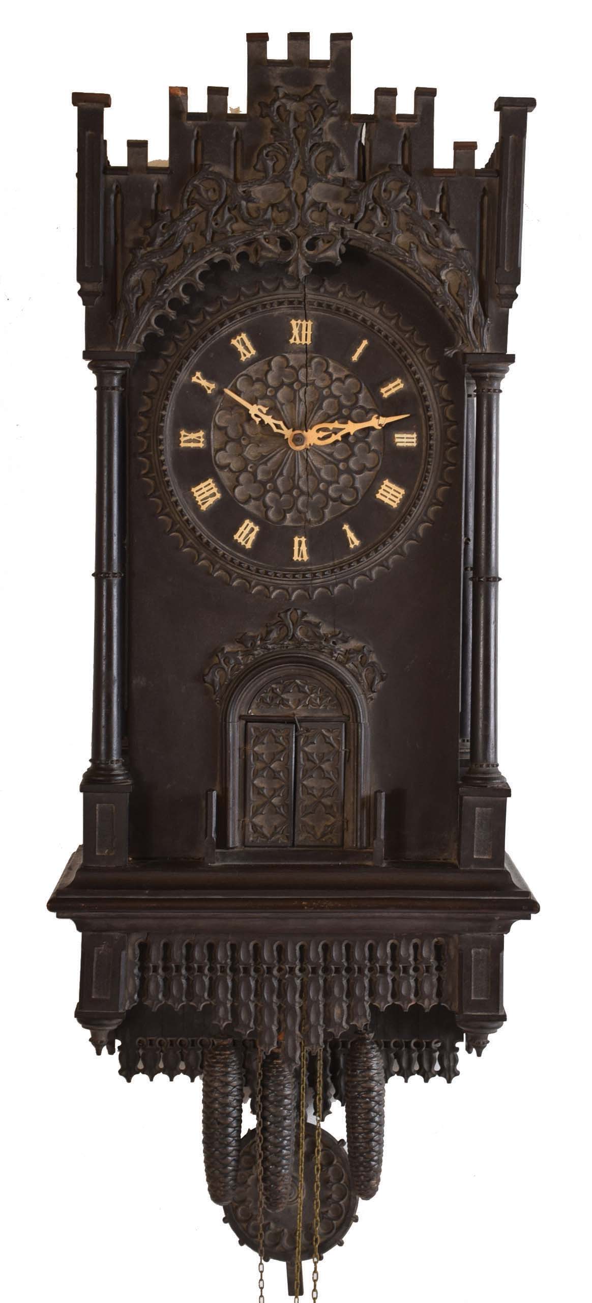 Trompeteruhren, or Trumpeter Clock, attributed to Emilian Wehrle, Germany, the ebonized, architectural case of Gothic design, with crenellated parapet, the front of which is adorned with applied rustic vine carving, the dial, doors, and base with various pierced, foil carvings, and with columns at the corners, case sides with pierced, arched access doors, Roman numeral wooden dial with blind, geometric, foil fret, pierced bone hands, three train, weight driven movement with wooden plates and brass wheels, and carved wooden pendulum, also with blind fret carving, music played on 6 pipes, the trumpeters emerging from behind the doors at the hour to play a tune — Antique Clocks Price Guide