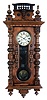 Clocks- 2 (Two) Vienna regulators, Germany, 8 days: (1) Junghans, Wurttemberg, time and strike, spring driven movement in a carved Alt Deutsch walnut case with barbell shaped glazed window in door, turned elements and pressed brass pendulum The dial is a cream enamel two part with Roman numerals. (2) Germany, time only, brass weight driven movement in a walnut case with two part white enamel dial and second's bit