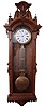 F. Kroeber & Co., New York, N.Y., "Regulator No. 27", jeweler's regulator wall clock, 8 day, time only, brass weight driven with Swiss pinwheel escapement timepiece movement, with a white enameled dial, a gridiron lyre pendulum and sweep seconds in a walnut case with burled accents and ornately carved top showcasing an urn in the center.