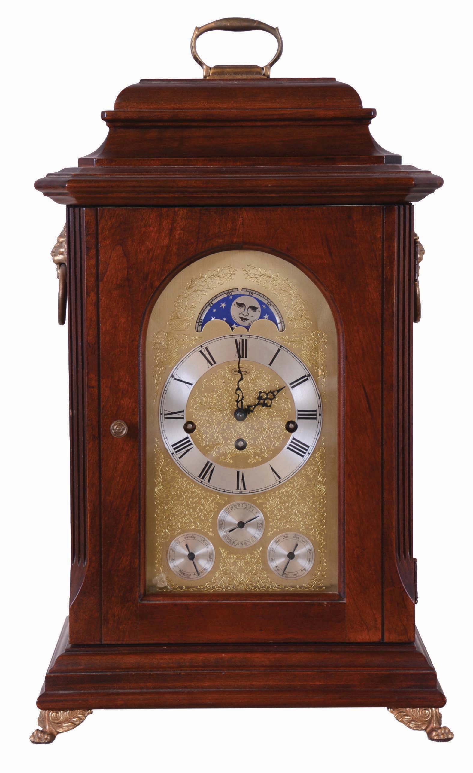 Unknown American mfg bracket clock, with Franz Hermle Westminster chime and calendar movement, and with rolling moon in the arch of the embossed dial. Case with mahogany finish, and with cast feet, handle and side lions. Day of week, date and month in English show on bottom dials. — Antique Clocks Price Guide