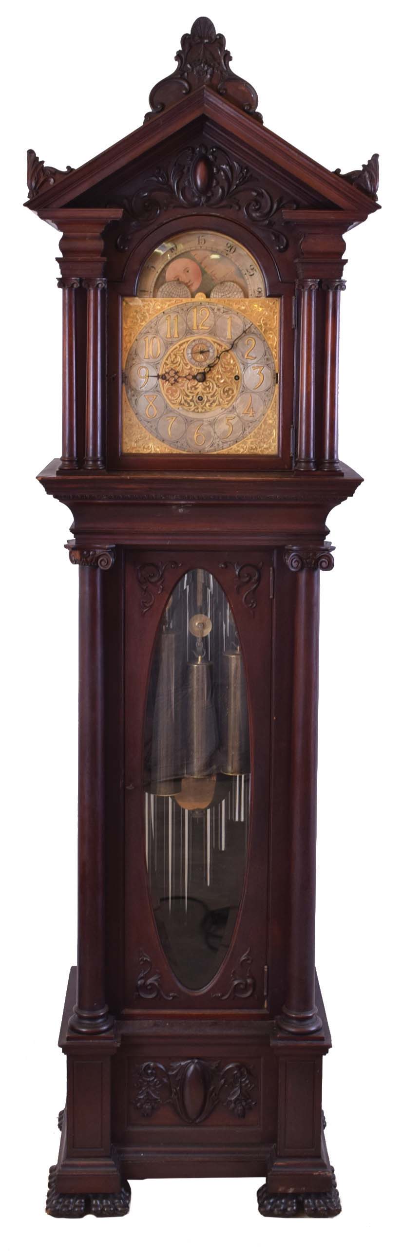 England tall clock with tubular bells retailed by Bigelow, Kennard &amp; Co., 8 day, time, strike and chime on 9 tubular bells playing Westminster and one other tune, three brass weight driven movement in a mahogany case with pediment top and side and center carvings. The tympanum above the dial has applied carved moldings, the hood door has double columns on each side with carved volute capitals over the trunk with full columns flanking beveled glass door with carved volute capitals resting on a base with applied carved moldings and paw feet. The brass dial has applied brass numerals over a silvered chapter ring and silvered second's bit, ornately engraved spandrels and dial center, moon phase, strike / silent and tune selectors. — Antique Clocks Price Guide