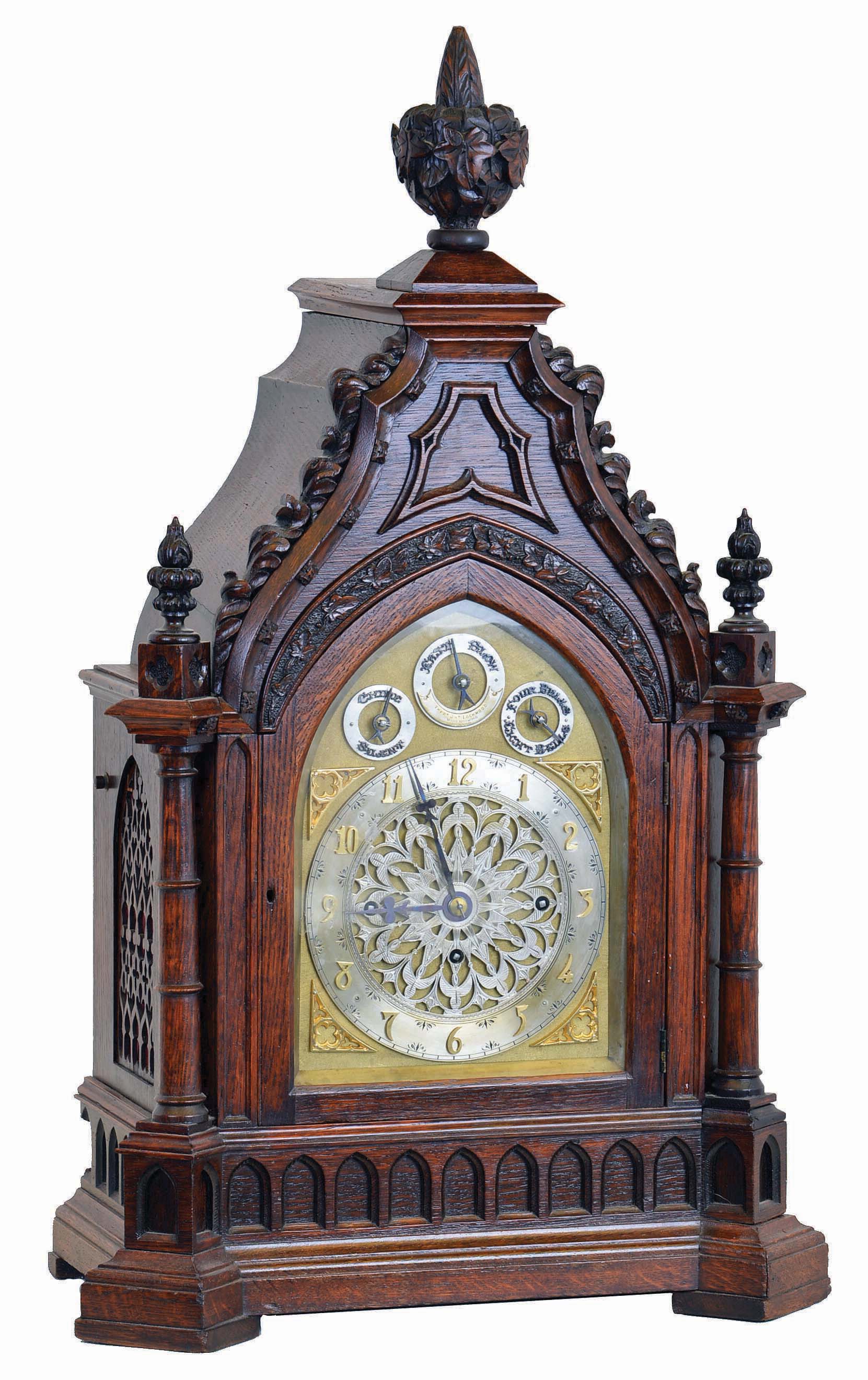 Frederick James Lockwood, West Norwood, London, large bracket clock in the Gothic style, carved oak case with buttress corners supporting turned columns, the molded base with lancet arch blind fret, lancet arch door below a carved lintel, the tympanum with applied, modified foil and hawksbill molding, all topped with foliate carving and decorative finials, case sides with pierced wooden frets, Arabic numeral silvered dial with gilt spandrels, with subsidiary dials for selecting chime tune, mode and regulation, blued steel hands, and substantial, 8 day, 3 train fusee movement, sounding the quarters on four or eight bells and counting the hours on a large gong, the back plate also signed, c1845 — Antique Clocks Price Guide