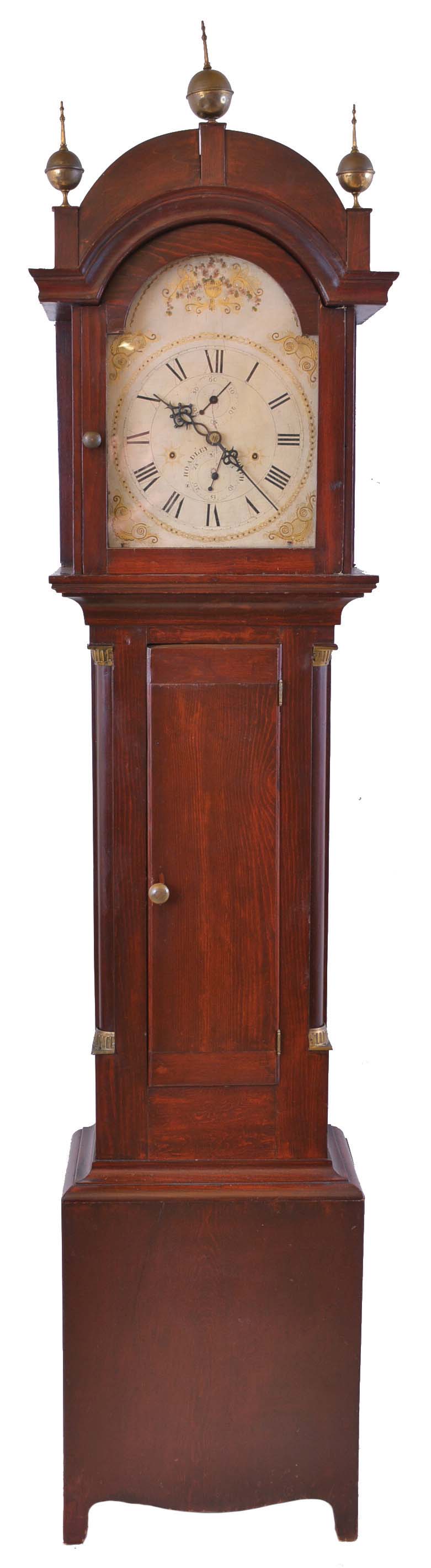 Silas Hoadley, Plymouth, Conn., tall clock, 30 hour, time and strike with calendar, weight driven, wooden works movement in a dark stained pine case with columns flanking trunk door and three brass finials. The wooden painted dial and pewter hands. — Antique Clocks Price Guide