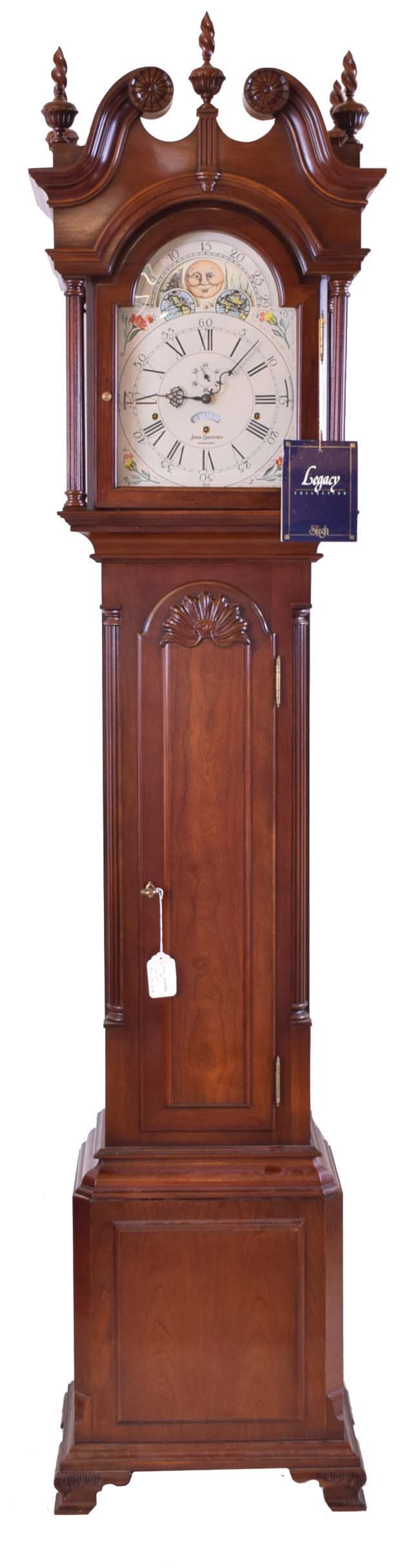 The Henry Ford Museum, Dearborn, Michigan reproduction John Goddard, Newport, Rhode Island, tall case clock, 8 day, time, strike and triple chime, weight driven movement in a mahogany case with five wooden finials, carved rosettes, fluted full columns on hood over Goddard style shell carving on trunk with fluted corner columns on double paneled base resting on ogee feet with moon phase dial — Antique Clocks Price Guide