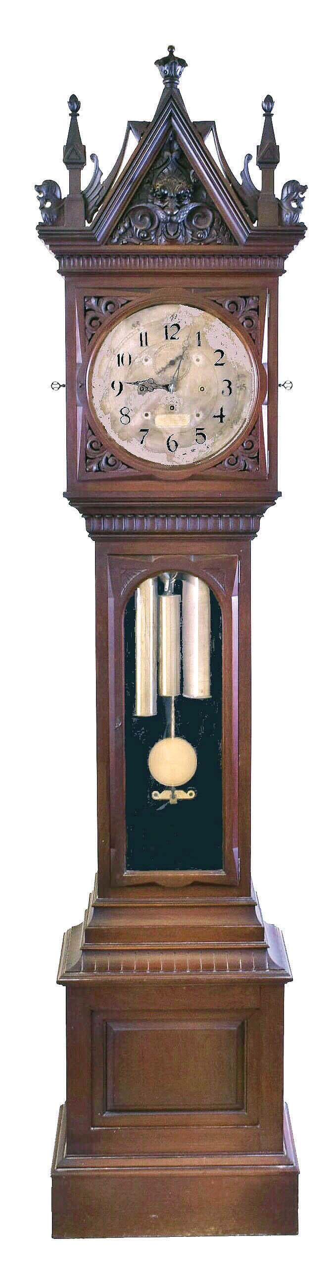 E. Howard &amp; Co., Boston, No. 77 hall clock with Westminster chimes, mahogany case, the molded base with inset panel, trunk door with fan carved corners and beveled glass, the interior lined with black flocked paper, and bonnet with carved grotesque mask, gryphons, and gothic style pinnacles, 14 inch, Arabic numeral silvered dial, blued steel English pattern hands, 8 day, three train movement with Graham deadbeat escapement, full Westminster chiming, stopwork on all trains, and counting the hours on a gong, brass weights, heavy brass pendulum with gilt cherry rod — Antique Clocks Price Guide
