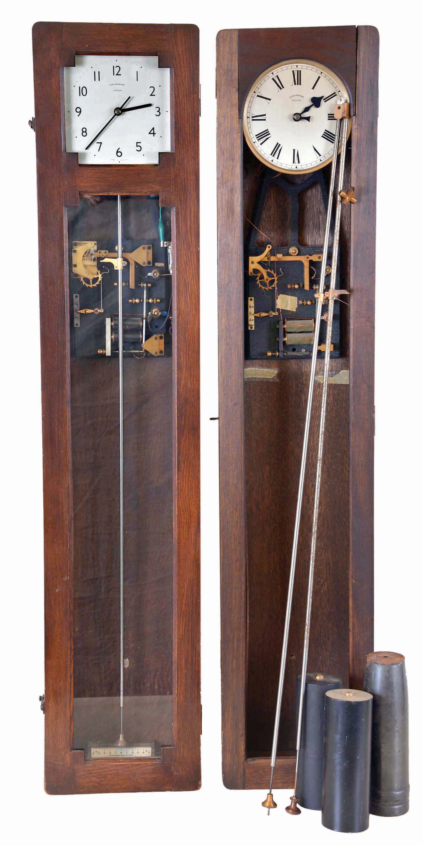 The Synchronome Co., Ltd., England, master clock, quarter sawn oak case, Arabic numeral metal dial, and pendulum with cylindrical ball, receiving impulse every thirty seconds from a falling gravity arm, together with another Synchronome master clock with mahogany case, Roman numeral silvered dial, and also with correct pendulum, plus a third pendulum — Antique Clocks Price Guide