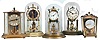 Clocks- 5 (Five) German 400 day brass and glass or "anniversary" clocks: Badiche with disk pendulum, early 20th century; later square carriage- style Schatz; 6 size Seth Thomas; Kieninger with white painted areas and original paperwork; floral enamel dial