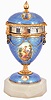 Switzerland, miniature urn form annular clock, the case with blue guilloche enamel and gilt molding, decorated with 7 paillon framed polychrome enamel portraits, the finial and stem with white enamel accents, and Roman numeral silvered dial, all on an octagonal, polished stone base, c1900