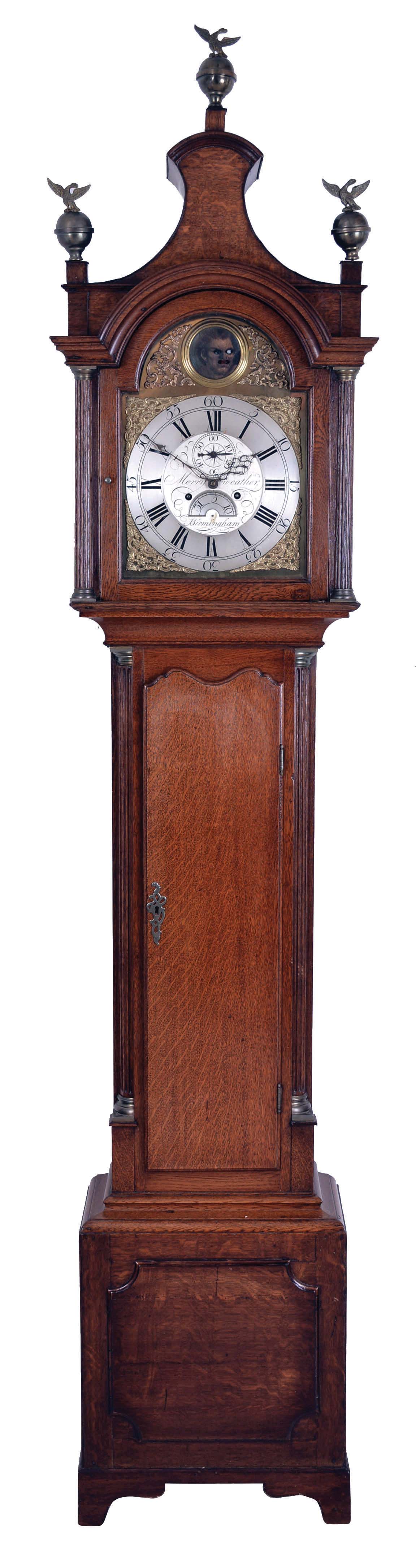 Merryweather, Birmingham, late 18th century tall clock with automata in the arch, the oak case with bracket feet, the base with thumb molded panel with incurved corners, trunk with engaged quarter columns and thumb molded door with oxbow and ogee shaped top, bonnet with break arch door, flanking columns, and pagoda top, composite dial with Roman numeral, silvered chapter ring, the signed, engraved center with calendar aperture below the center arbor, and the arch with disc, having an oil painting of a deranged looking fellow with wagging tongue and moving eyes, 8 day, weight driven time and strike movement, cast iron weights, and pendulum with brass clad ball — Antique Clocks Price Guide
