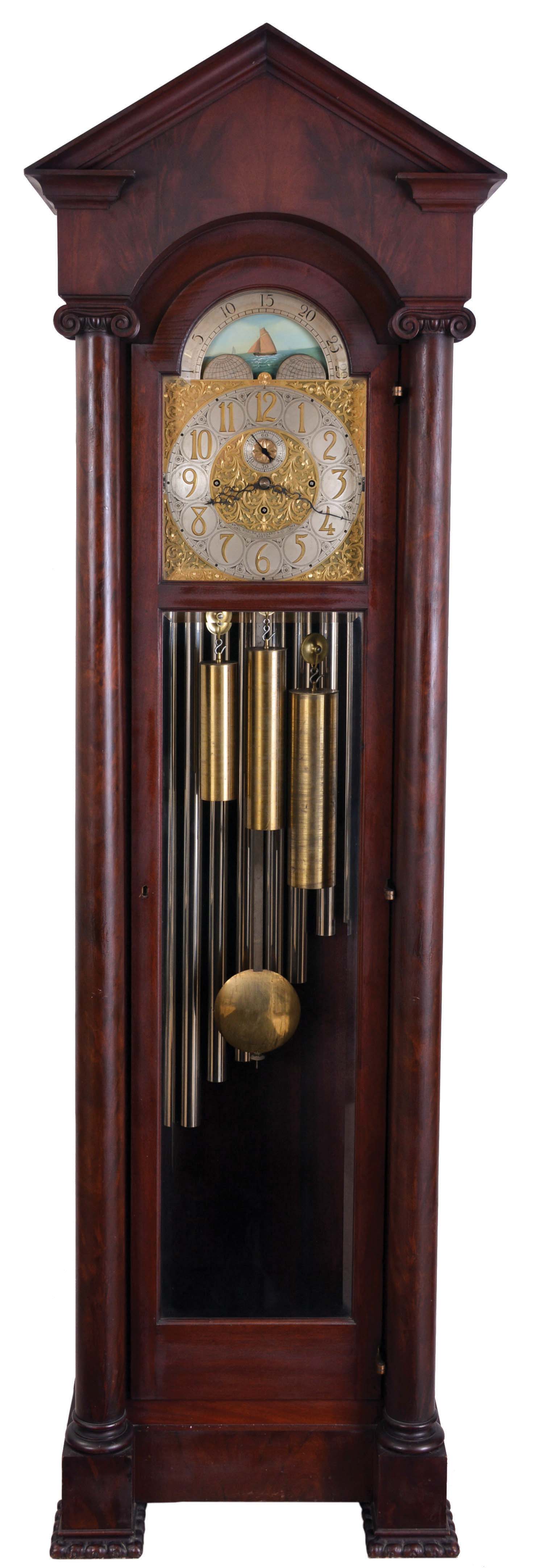 English, 3-train, 9-tube, brass dial tall clock, retailed by Bigelow, Kennard &amp; Co., mahogany case with pediment top, door with two bevelled glasses, and with flanking columns having carved Ionic capitals, and resting on carved feet, composite dial with aplied numerals, silvered chapter ring and seconds bit, and displaying the phases of the moon, 8 day, quarter chiming, weight driven movemen — Antique Clocks Price Guide