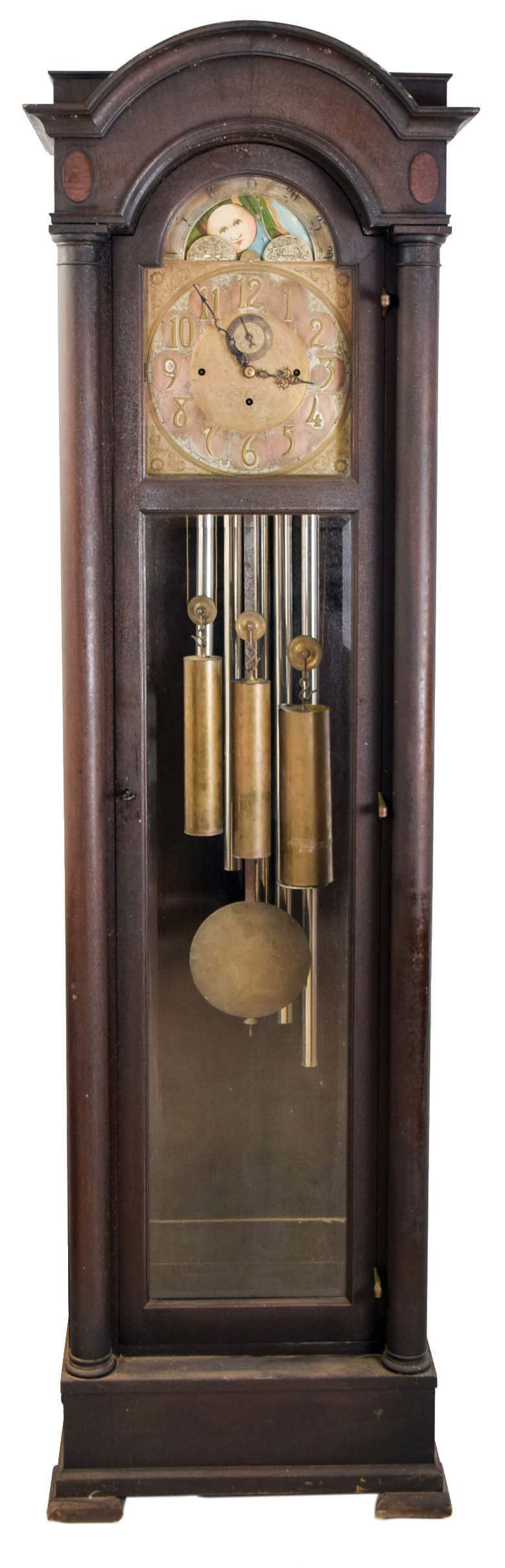 Colonial Manufacturing Co., Zeeland, Michigan, tall clock, quality German-made 8 day, time, strike three brass weight driven movement, with Westminster chime on tubes, in an inlaid mahogany case with full length full columns flanking a full length door with lower beveled glass, brass dial with moon phase and engraved spandrels. — Antique Clocks Price Guide