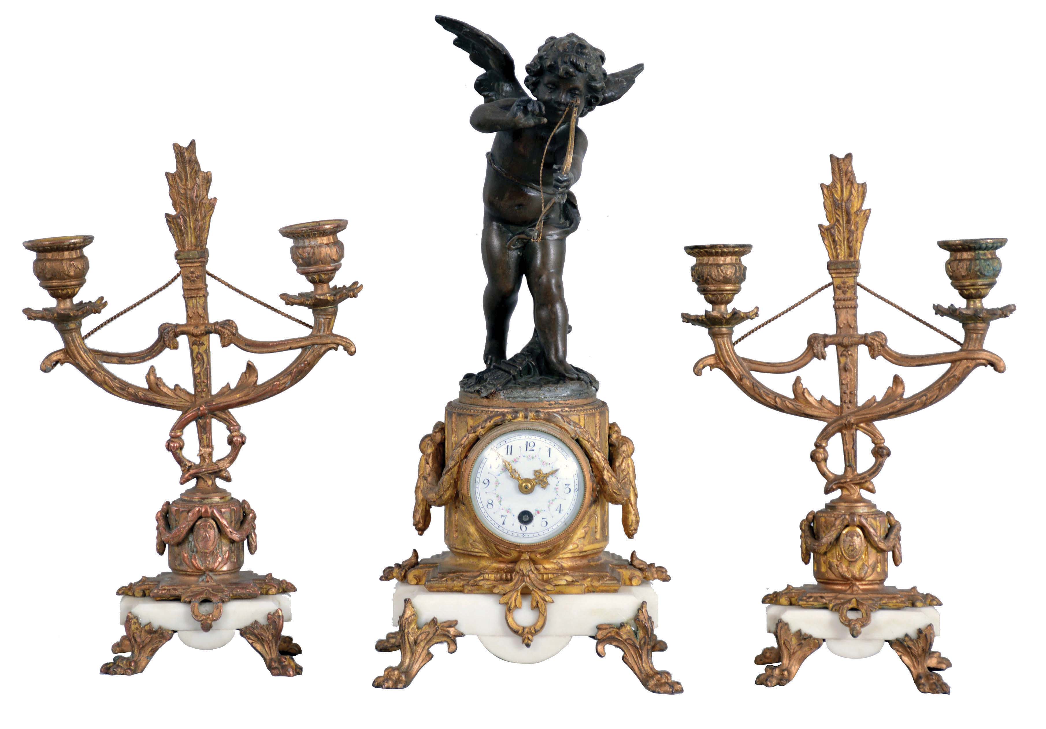 Mini clock set- France, 8 day, time only balance wheel movement behind white enamel dial with polychrome floral design on a white marble base with gilt claw feet supporting a cast fluted pedestal, surmounted by a patinated spelter figure of Cupid drawing his bow. Set is completed by two matching candelabra, both holding two candles each. — Antique Clocks Price Guide