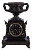 Charles Pickard, Paris, figural mantel clock, 8 day, time and strike movement by Japy Freres, patinated cast brass feet with human faces supporting a black slate case and dial with incised designs and numerals, surmounted by a handled urn displaying 8 human faces around the outside, c1880.