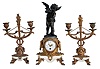 Mini clock set- France, 8 day, time only balance wheel movement behind white enamel dial with polychrome floral design on a white marble base with gilt claw feet supporting a cast fluted pedestal, surmounted by a patinated spelter figure of Cupid drawing his bow. Set is completed by two matching candelabra, both holding two candles each.