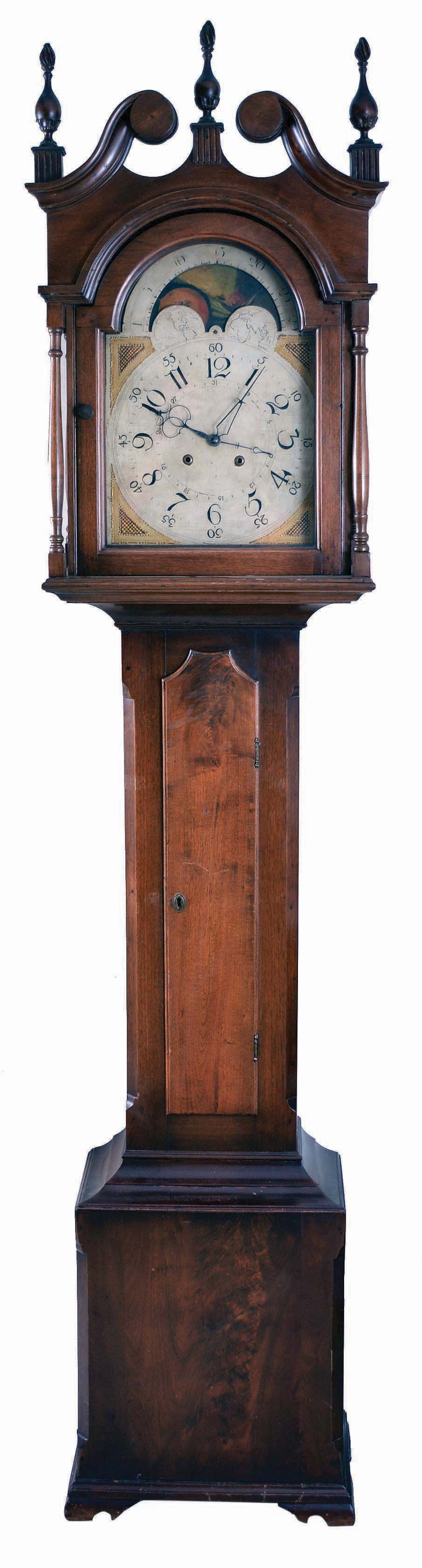 Pennsylvania, tall case clock, 30 hour, time and bell strike, single weight driven movement in a walnut case with broken arch top, three wooden flame finials, four turned columns at bonnet corners, over cove molded trunk with shaped door top, and crotch walnut base resting on ogee bracket feet. The painted metal dial retains its originalpaper label, "CURTIS' MANUFACTORY FOR PATTON &amp; JONES, PHILADELPHIA" and has calendar hand off center arbor, moon phase with interesting burning ship scene. — Antique Clocks Price Guide