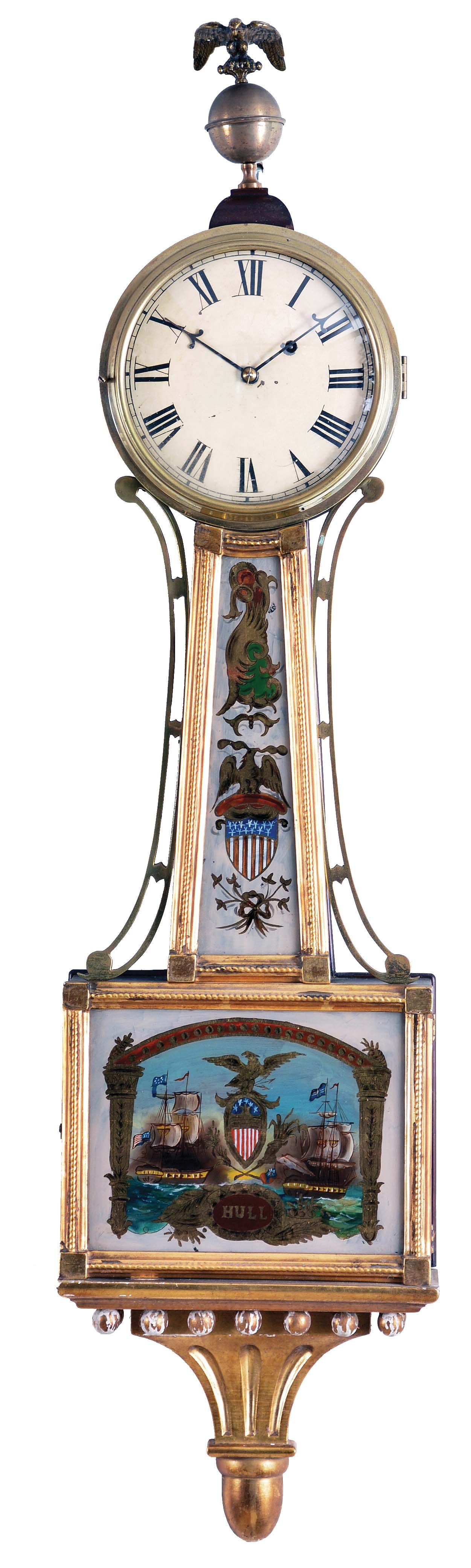 Bench-made Patent timepiece or "Banjo" Clock, with mahogany case, brass bezel opens to the roman numeral dial surmounted by a ball and eagle finial, gilded rope molded frames for the reverse-painted glasses, the lower depicting and inscribed "Hull" with central shield and eagle pendulum aperture, the waist glass with similar patriotic depiction of a Federal shield and eagle amidst decorative scroll work in gold, red, green and white, the whole resting on a carved and gilded pedestal at the base with acorn drop, eight day time-only movement with recoil escapement, lead weight and pendulum bob and iron rod. — Antique Clocks Price Guide