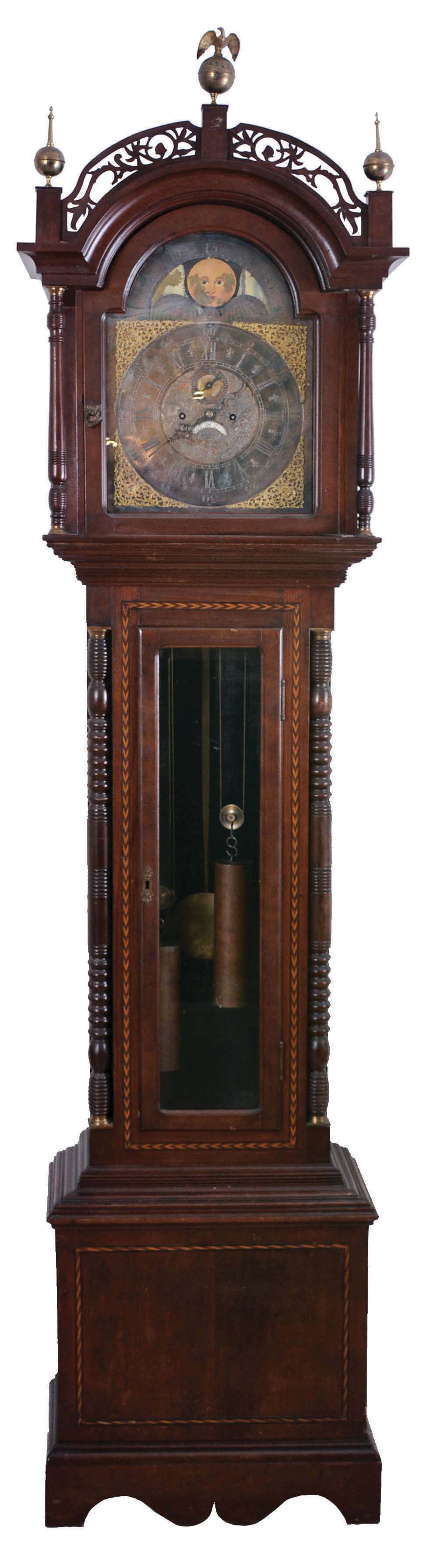 Ty Burtt, England, tall case clock, 8 days, time and gong strike, brass weight driven movement in an inlaid cherry case with with fret work hood, brass finials including eagle center, full turned columns flanking hood, beveled glass trunk door flanked by full columns and applied bracket base. The brass dial has silvered chapter ring, applied brass numerals, moon phase and date calendar — Antique Clocks Price Guide