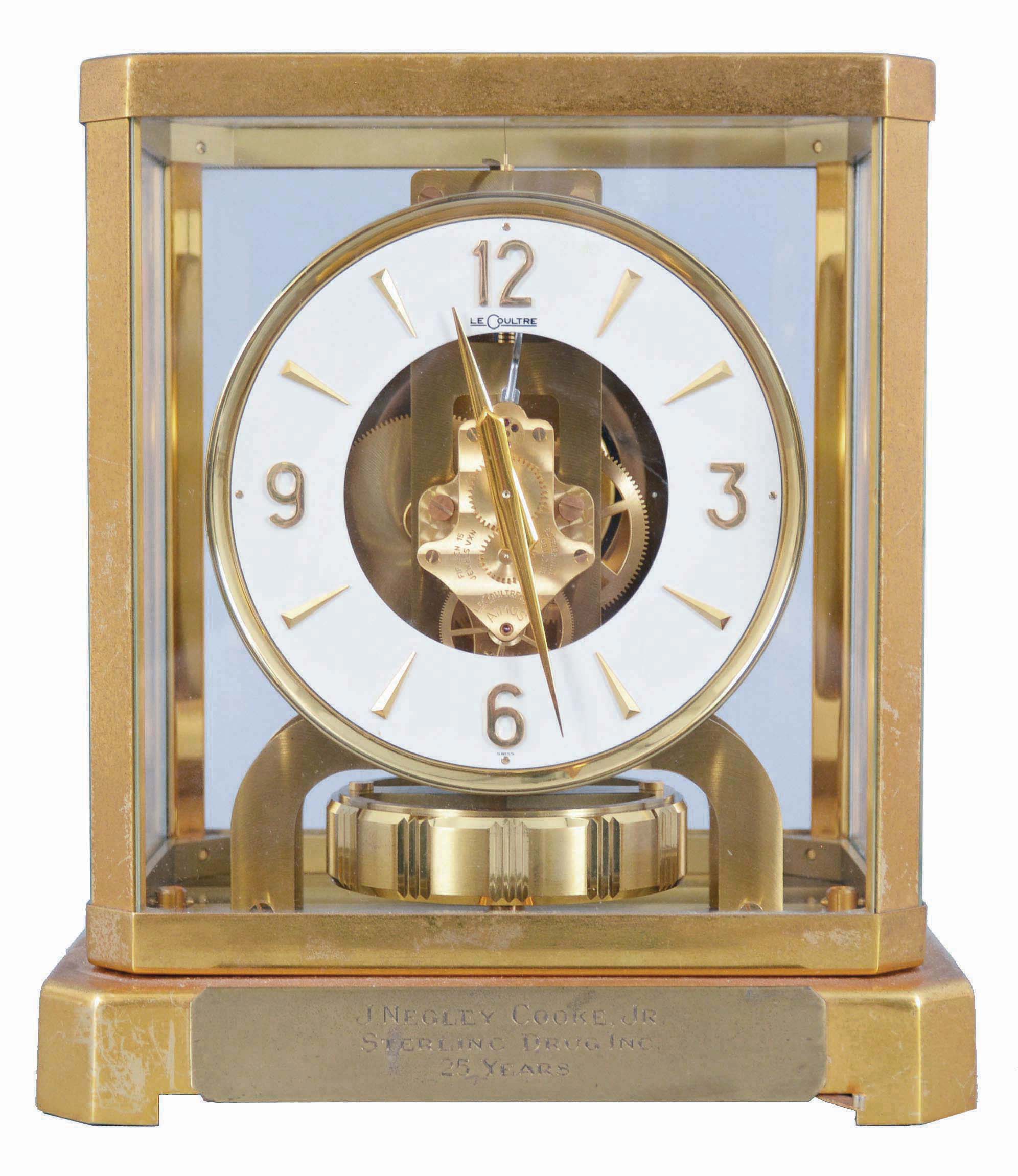 Jaeger- LeCoultre, Switzerland, "Atmos" clock, 15 jewel, caliber 528-8 movement, gilt torsion pendulum, round white painted dial with applied gilt Arabic numerals and arrow markers, gilt hands, all contained in a glazed rectangular case with dedication plaque, serial #128209, c1960. — Antique Clocks Price Guide