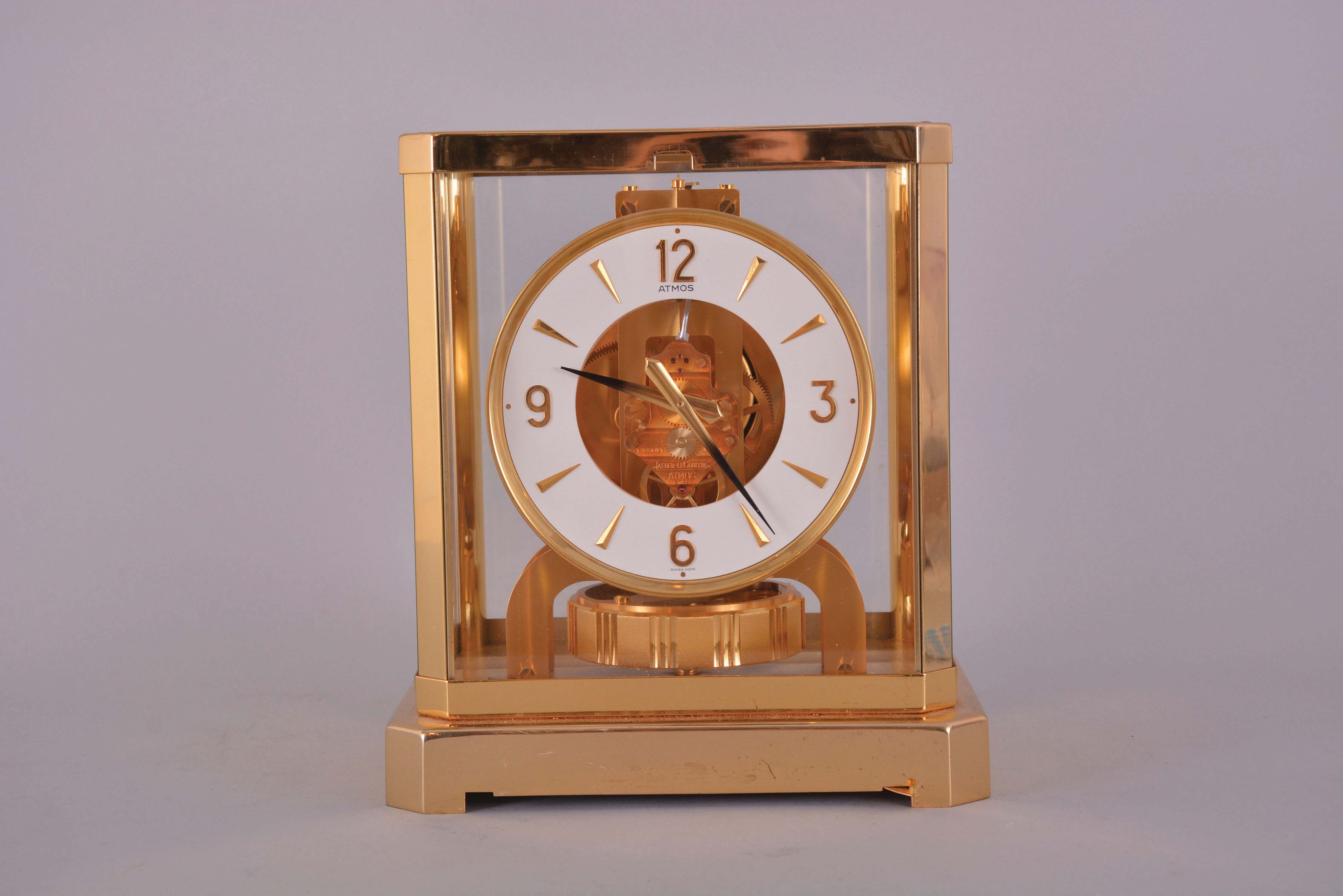 Jaeger- LeCoultre, Switzerland, "Atmos" clock, 15 jewel, caliber 528-8 movement, gilt torsion pendulum, round white painted dial with applied gilt Arabic numerals and arrow markers, gilt hands with blackened tips, all contained in a glazed rectangular case, movement serial #563139, c1983. — Antique Clocks Price Guide