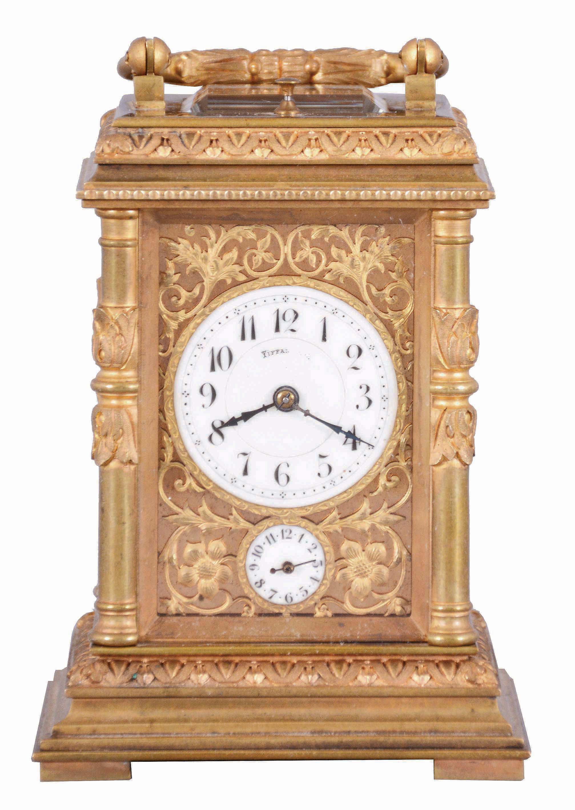France, for Tiffany &amp; Co., a Pillars style, petit sonnerie striking carriage clock with repeat, the glazed, gilt case with bright and matte surfaces, the base and cornice with cavetto and egg and dart moldings, the corners with acanthus decorated columns, and carrying handle also with foliate ornament, Arabic numeral white enamel dial with fretted, matte gilt foliate mask against a bright gilt background, blued steel distaff hands, 8 day time, strike, and alarm movement with lever platform, sounding petit sonnerie quarters in passing, with grand sonnerie repeating on demand, the base with strike/ silent lever — Antique Clocks Price Guide