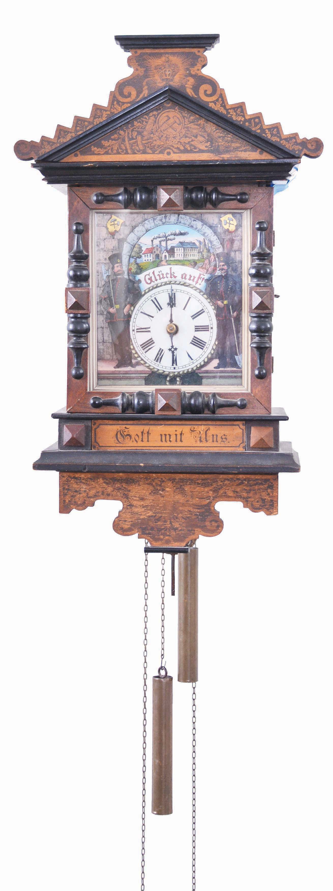 Black Forest, wall clock, 30 hour, time and strike, weight driven wood plate movement in a wood case with ebonized trim, polychrome back painted glass dial featuring two men in 18th century minersi uniforms, a foundry scene, and the words "Gl,ck auf!" ("good luck") -- a greeting German miners used when wishing one another luck. The transferred design on the crest has related imagery including the crossed hammer and pick, a pan, shovel, and lantern. Below the dial on the case are the words "Gott mit uns" ("God with us") which was often used on Prussian heraldry as an expression of unity. On the bracket at the base of the clock is an eagle typical of the Prussian coat of arms. — Antique Clocks Price Guide