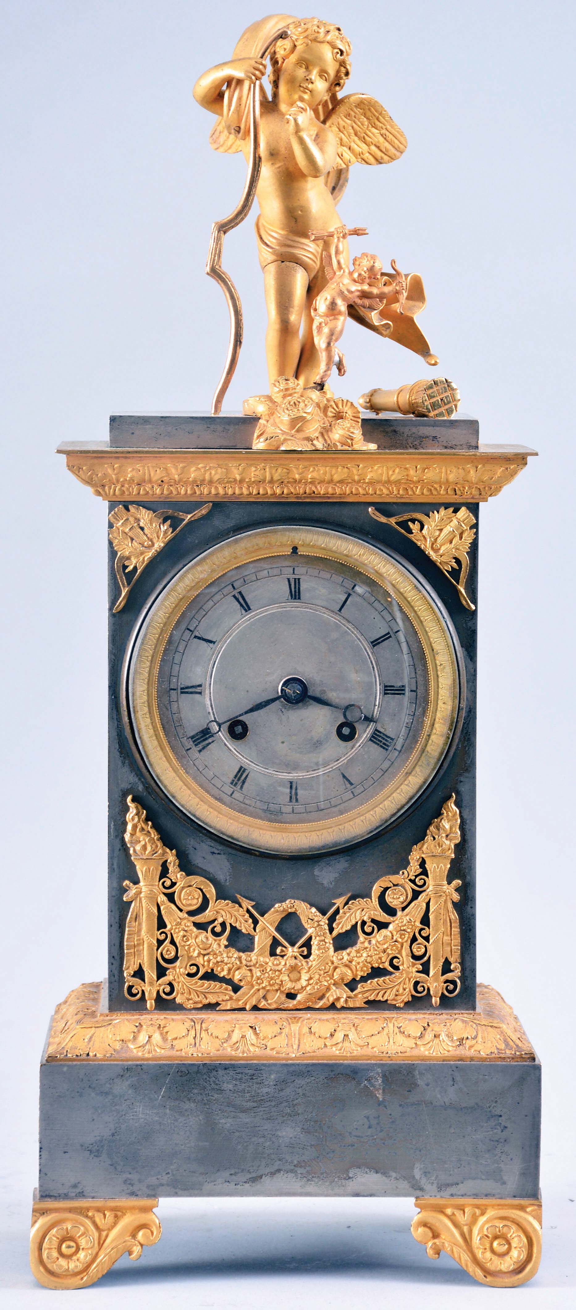 France, an attractive architectural mantel clock with animated figure, gilt and silvered bronze case, the rectangular base on gilt, scroll feet with Grecian ornament, the mid section also with cast ornament surrounding the Roman numeral silvered dial, and top with deeply molded, ornamental cornice, surmounted by a figure of Cupid with his bow and quiver, now with a smaller cupid at his feet, above a cluster of flowers, and attached to a wire linked to the pallet arbor, rocking to and fro as the clock runs, 8 day, time and strike pendule de Paris movement signed "Rodel", with silk thread suspension — Antique Clocks Price Guide