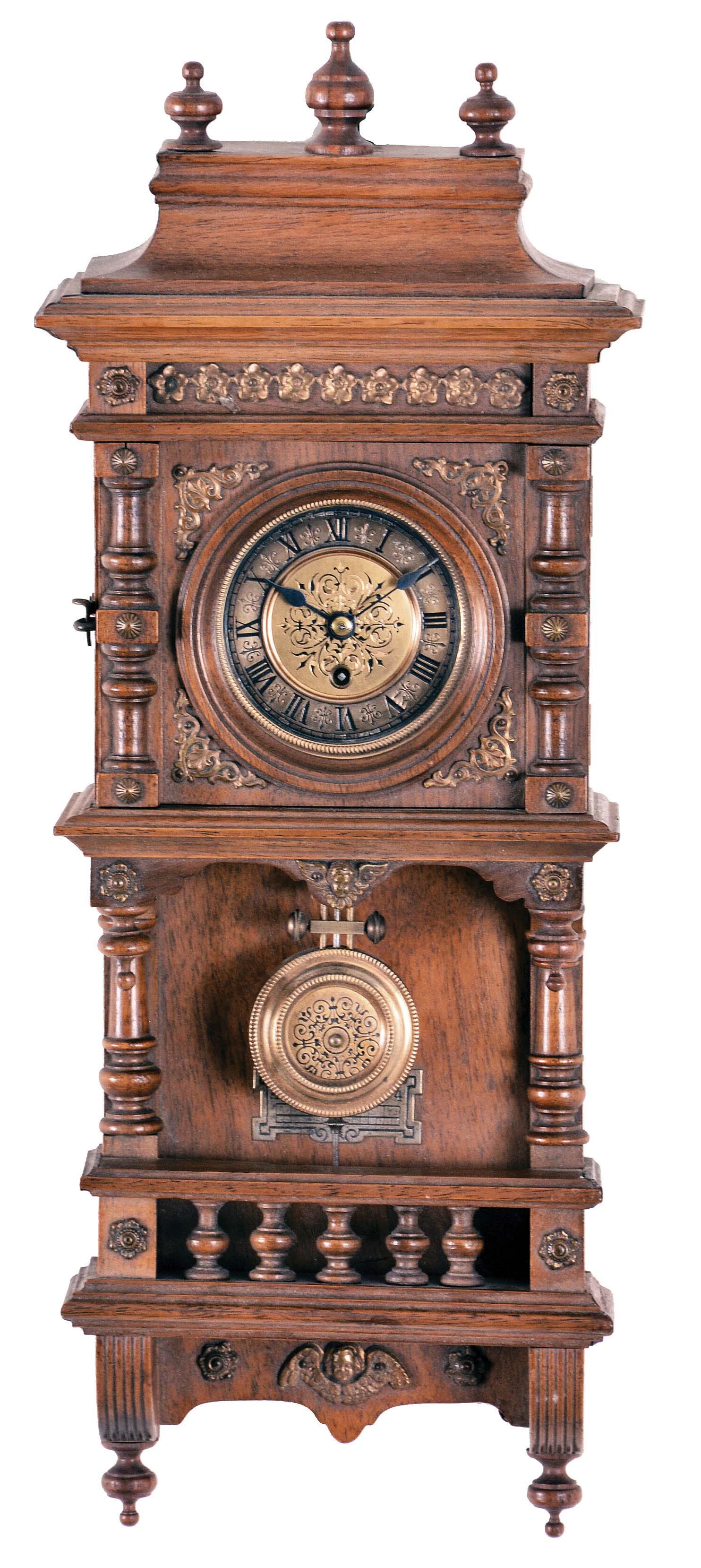 Germany, a miniature "Freischwinger", the walnut case with deeply molded top, recessed frieze with applied brass ornament, the door also with applied, split turnings and brass ornament, and open well with balustrade and supporting brackets, Roman numeral brass dial with engraved center, blued steel hands, 8 day timepiece movement with deadbeat escapement, and brass pendulum, with ornament matching the dial — Antique Clocks Price Guide