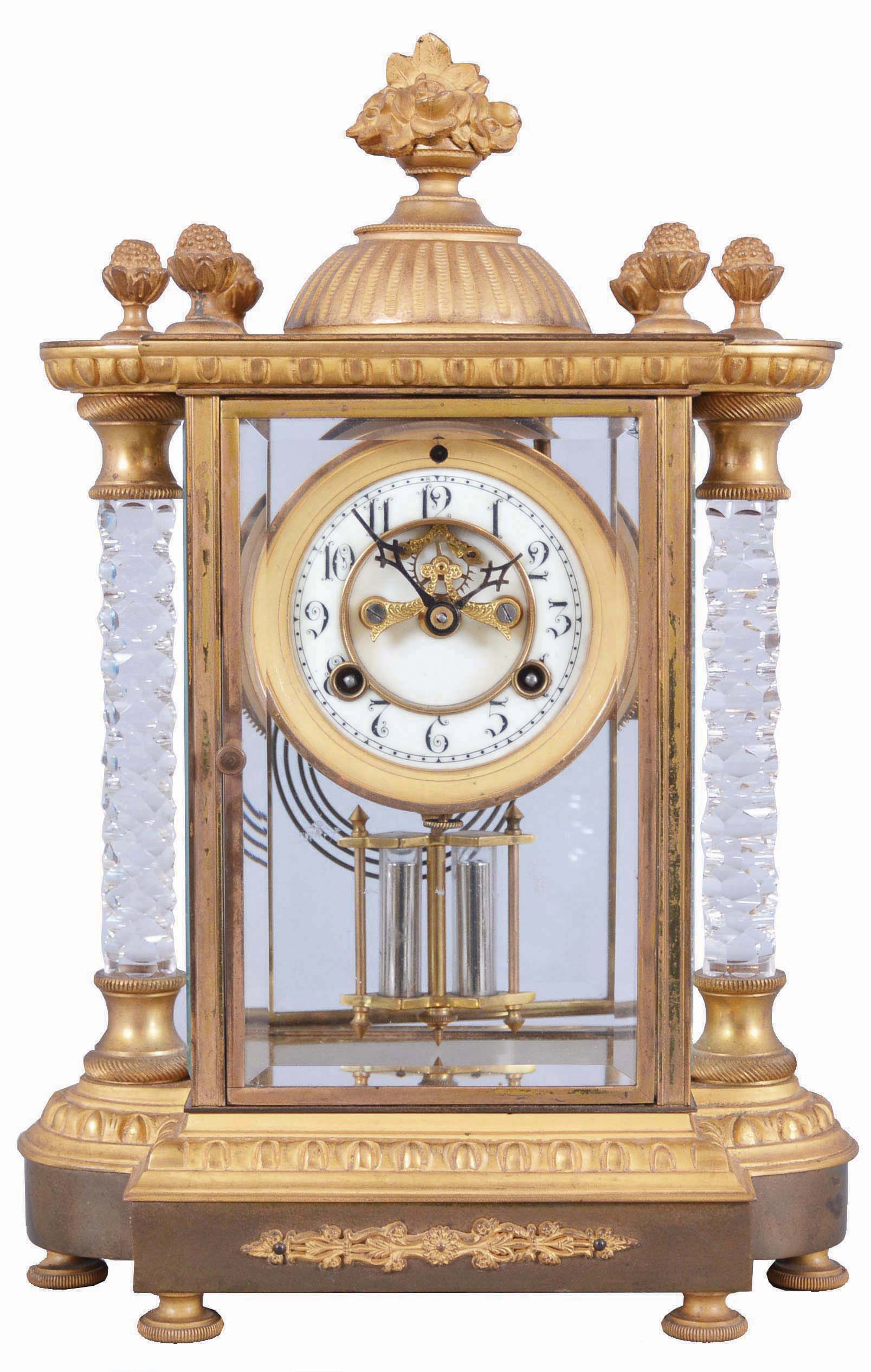 Waterbury Clock Co., Waterbury, Conn., "Orne" crystal regulator, 8 day, time and strike, spring driven movement with visible Brocot escapement in a gold plated case with two cut glass columns, white porcelain dial, and simulated mercury pendulum. — Antique Clocks Price Guide