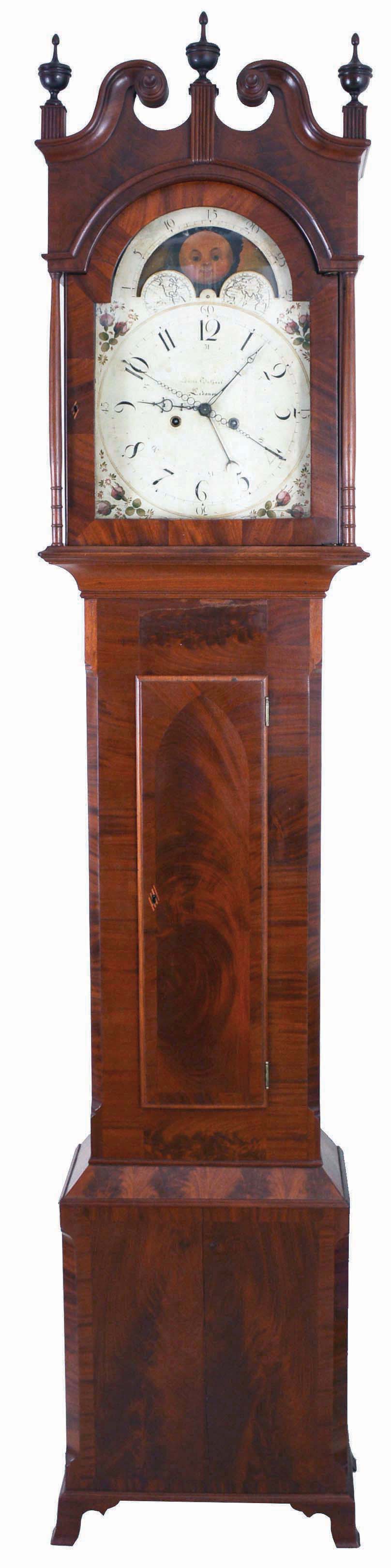Jacob Guthart, Lebanon, Pennsylvania, tall case clock, 8 day, time, strike and calendar with four hands off of center arbor, weight driven movement in a mahogany veneer case with a broken arch top, three wooden finials, four turned full columns over cove molded and chamfered sides flanking crotch mahogany trunk door all resting on French feet. The painted metal dial has maker's signature, moon phase and sweep seconds. — Antique Clocks Price Guide