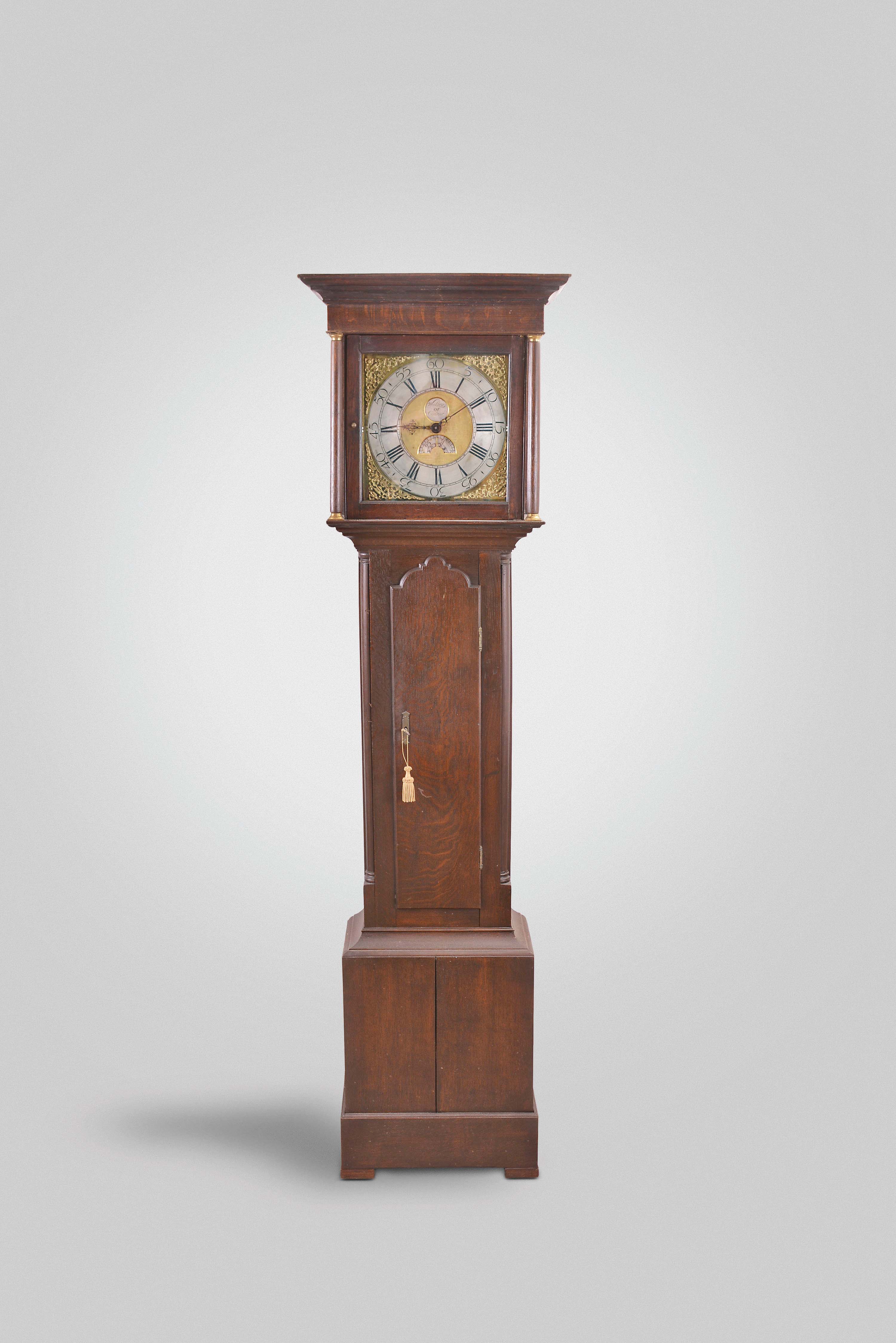 Woolley of Codnor, England, tall clock, 30 hour, time and strike, endless chain weight driven movement in an oak case with full columns topped by brass capitals flanking hood. The brass dial has silvered chapter ring, maker's signature on silvered disc and silvered calendar disc with serpentine hands. — Antique Clocks Price Guide