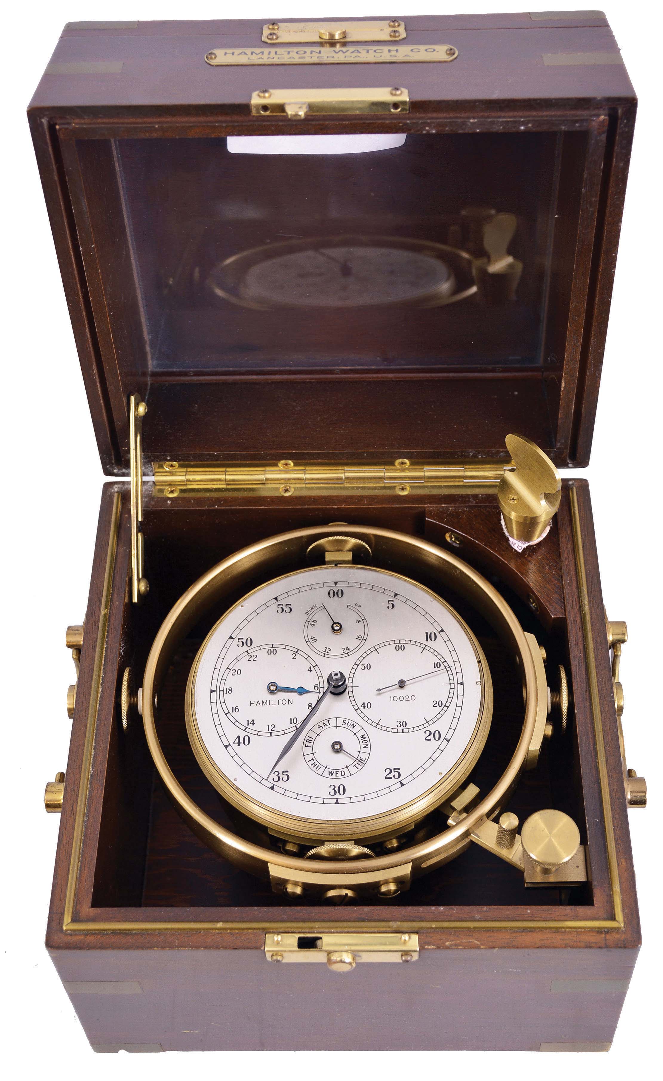 Hamilton Watch Co., Lancaster, Penn., model 21 marine chronometer, later converted to resemble the model 221, four orbit chronometer, 14 jewel key wind and set, straight line damascened nickel plate movement, with spring detent escapement and large, monometallic balance and helical balance spring, Arabic numeral metal dial with outer minute chapter, and subsidiary dials displaying day of the week, hours, seconds, and power reserve, black painted steel spade and poker hands, with gimbaled brass bowl, and mounted in a mahogany box with brass furniture, serial #2E10020 — Antique Clocks Price Guide