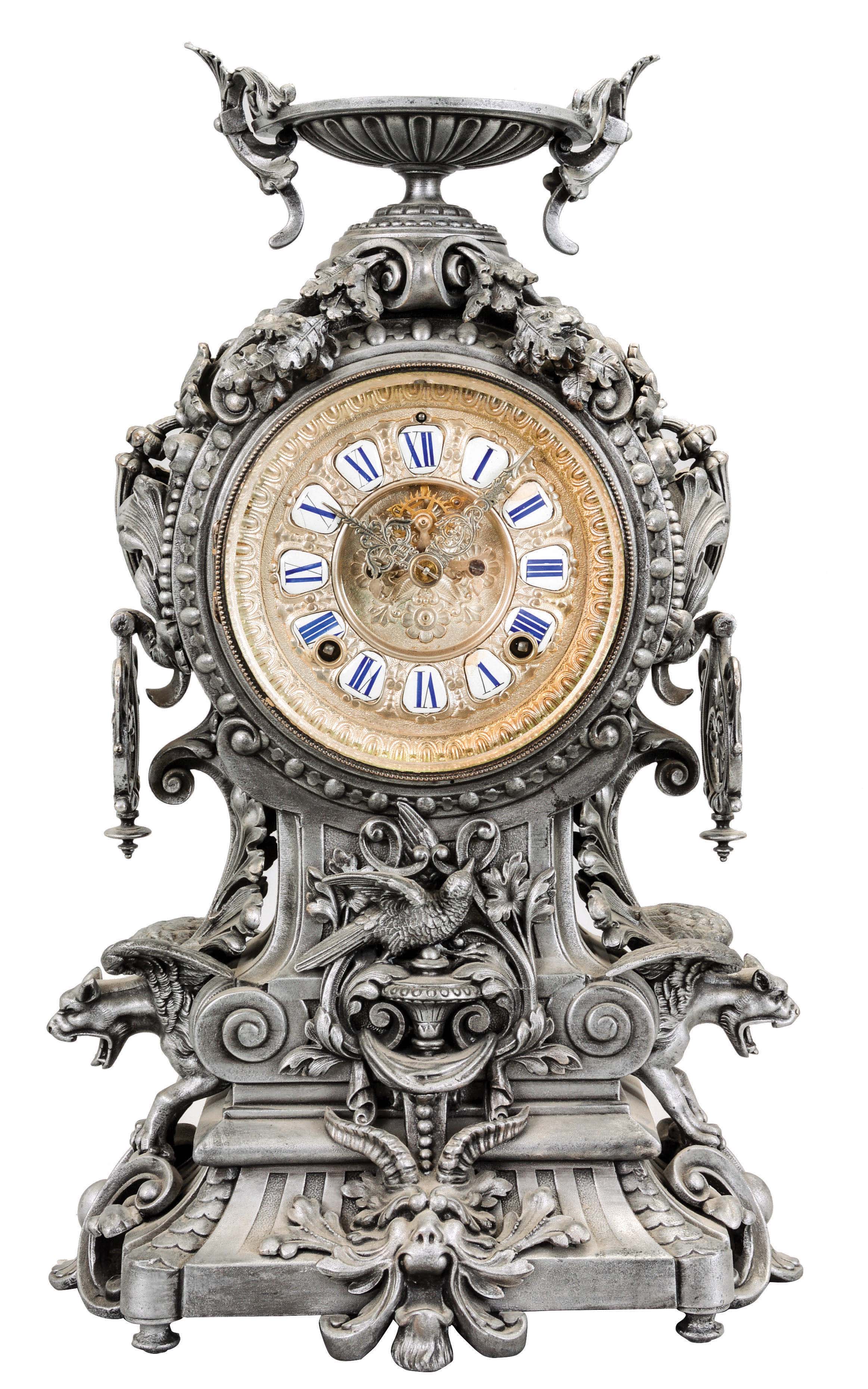 Ansonia Clock Co., New York, "Franconia" mantel clock with an 8 day spring driven time and strike movement with visible escapement and a cartouche dial in a silvered spelter case featuring flying gargoyles to the sides, a bird below the dial and profuse scrolls and swirls, surmounted by a winged urn. — Antique Clocks Price Guide