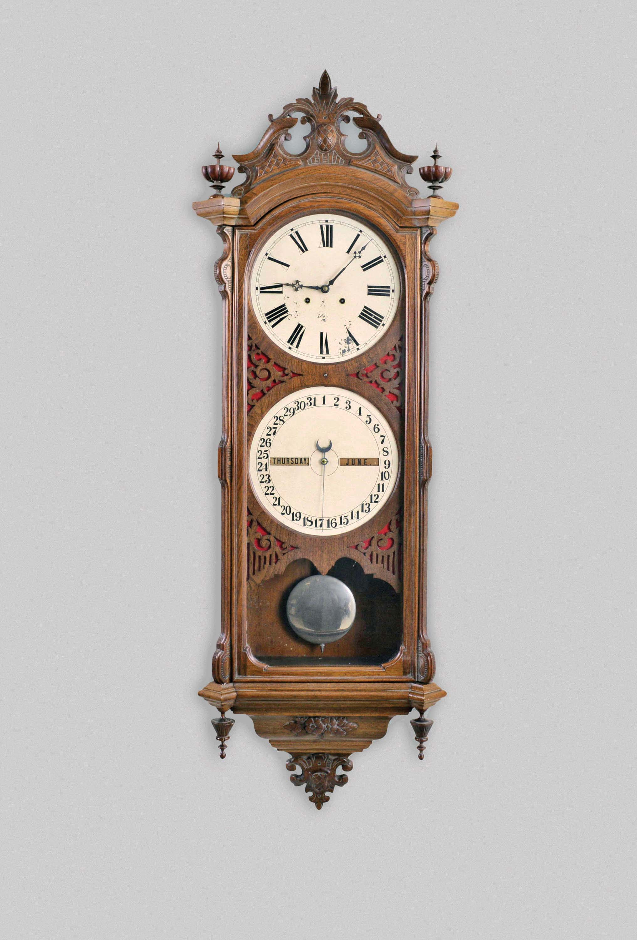 Ithaca Calendar Clock Co., Ithaca, New York, "No. 0 Bank", hanging 8 day, timepiece with perpetual calendar, weight driven movement in a walnut case with a carved pediment top, carved base and upper and lower finials with painted metal dials — Antique Clocks Price Guide