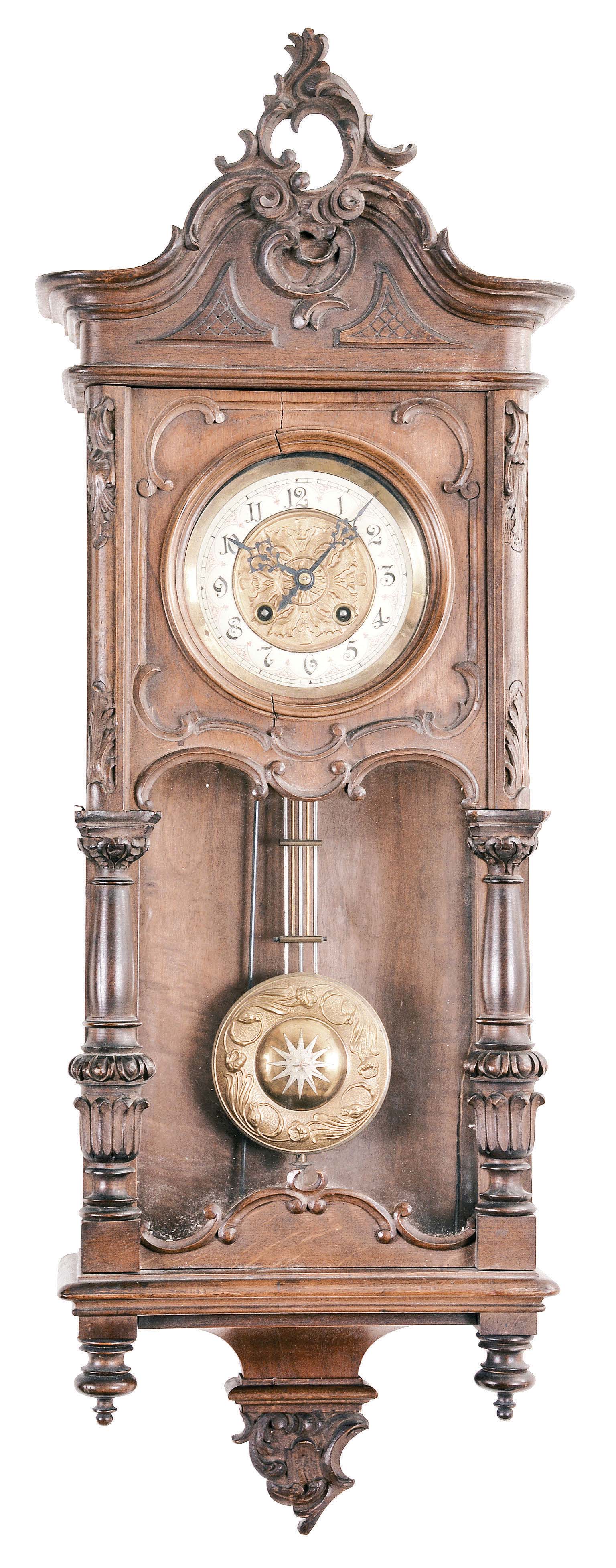 Gustav Becker, Freiburg, Germany, Vienna style wall clock, 8 day, time and strike (on a single chime rod), spring driven movement in a second Baroque style walnut case with short tapered columns and carved crest, embossed brass pendulum, cream porcelain dial and blued steel hands. — Antique Clocks Price Guide