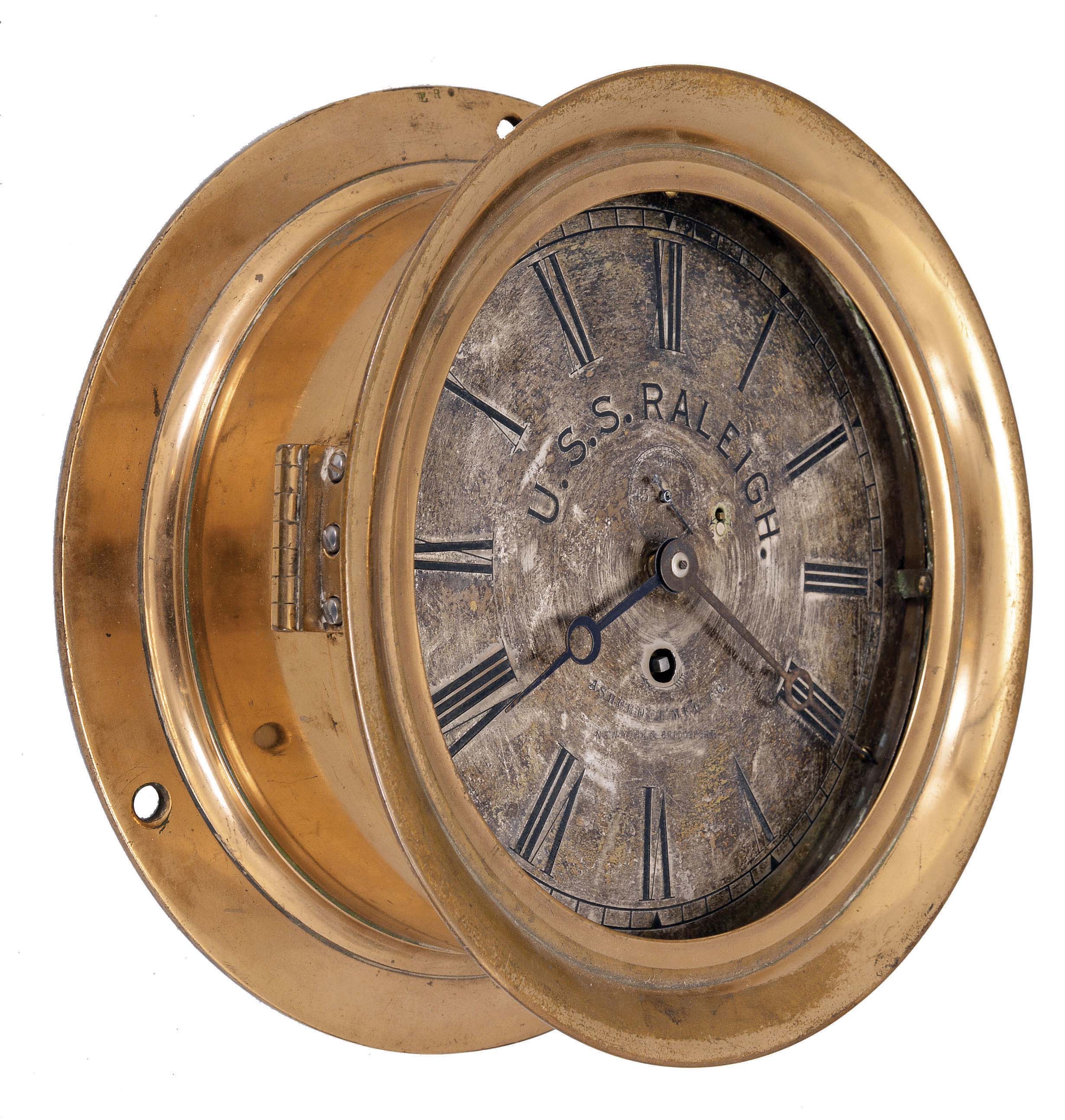 Chelsea Clock Co., Boston, Mass., for Ashcroft Mfg. Co., New York, deck or engine room clock, 8 day, time only, spring-driven jeweled balance wheel movement in a red brass case with hinged locking bezel, 8 inch silvered dial with with Roman numerals, an early Ashcroft trademark, and large letters reading "U.S.S. RALEIGH", black steel hands. — Antique Clocks Price Guide