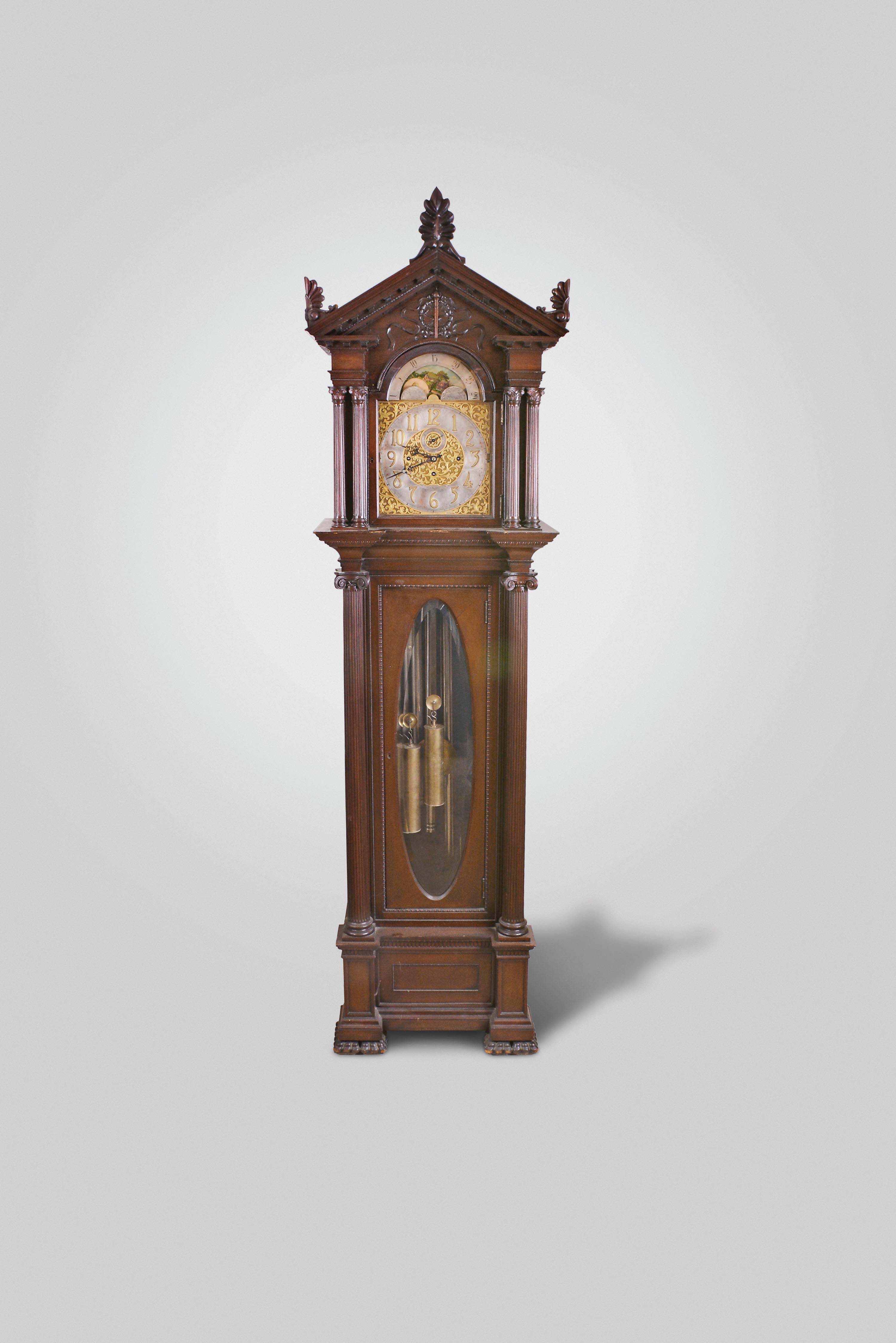 Herschede Hall Clock Co., Cincinnati Ohio for A.E. Siedle, Pittsburgh, Pennsylvania, "Pattern No. 99" hall clock, 8 day, time, strike and chime on five tubes signed Herschede Hall Clock Co., brass weight driven German movement in a carved mahogany case with full reeded Corinthian columns on the hood (in tandem) and the trunk door, beveled glasses on sides of hood and oval trunk door, carved large paw feet and trim on gabled top. The brass dial is signed by Pittsburgh retailer and has moon phase, silvered chapter ring with applied brass numerals and chime / silent and strike / silent selectors. — Antique Clocks Price Guide