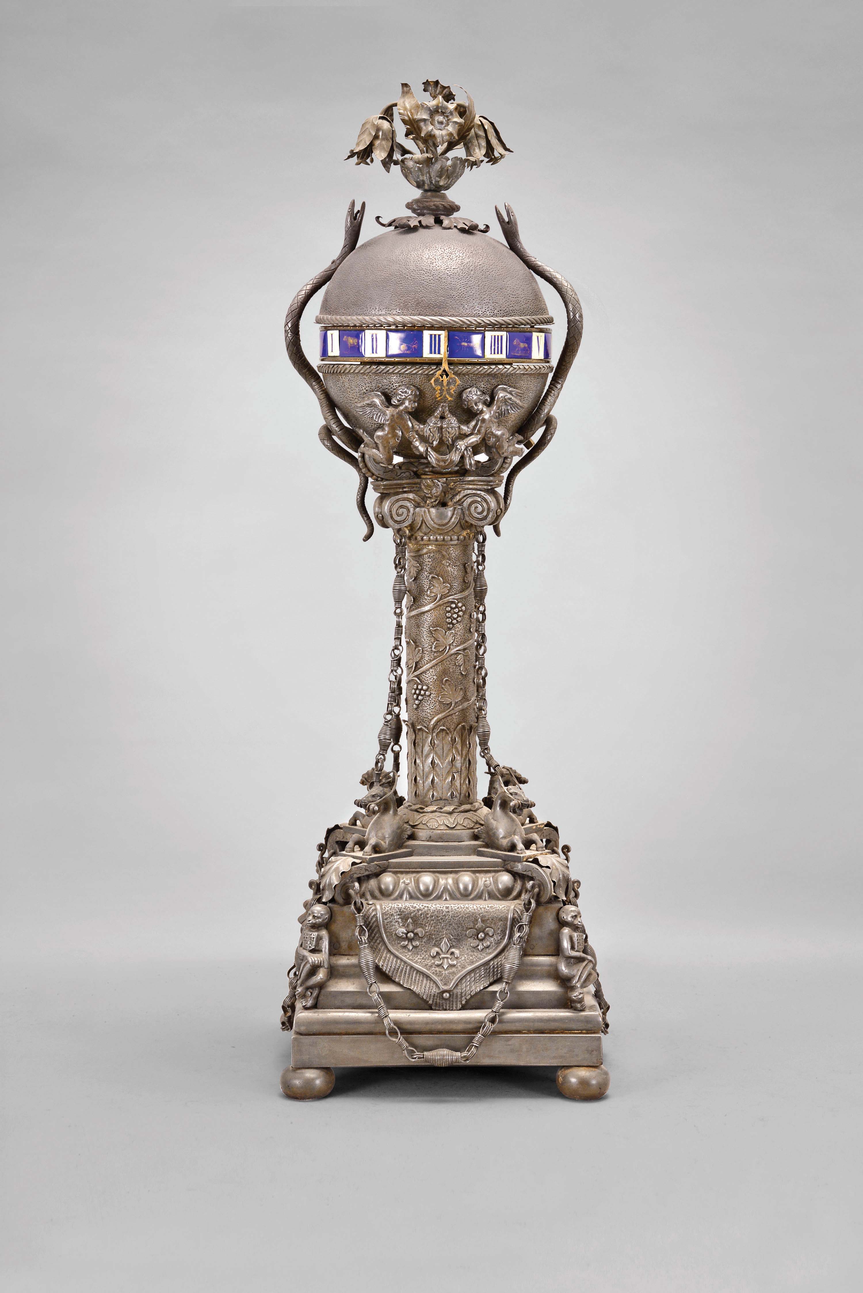 France, an unusual sheet iron annular clock, square, stepped, molded base on compressed ball feet and ornamented with seated monkeys, fleur de lis banners and egg and dart moldings below a waterleaf and grapevine decorated column, the base with four, addorsed, winged horses, and capital with volutes, surmounted by a sphere with foliate finial, flanking serpents, two putti holding the pointer and concealing the winding holes and crutch, the sphere containing the 8 day, two train, Japy Freres movement with Roman numeral, blue and white enamel annular dial, the numerals alternating with the signs of the zodiac — Antique Clocks Price Guide