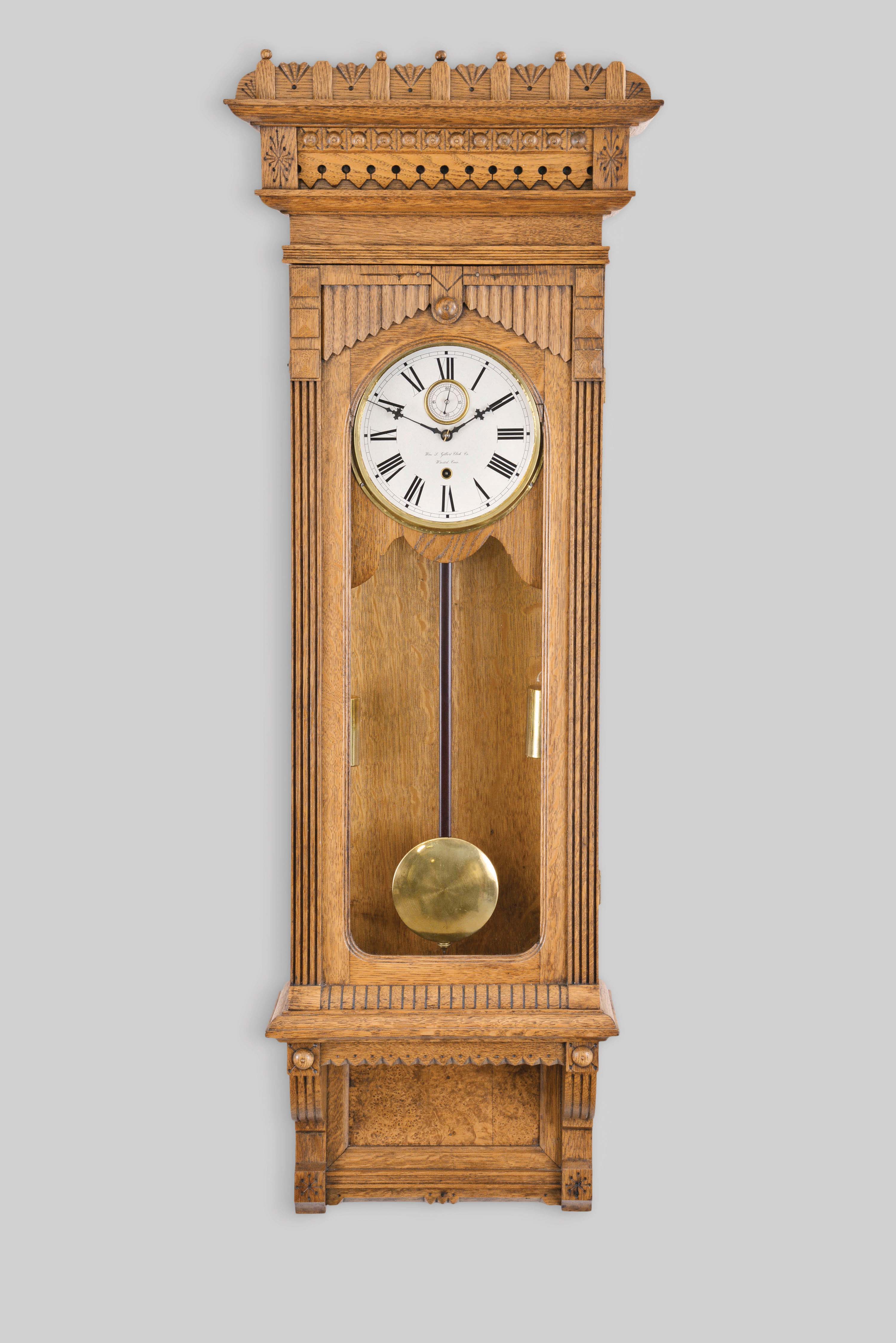 William L. Gilbert Clock Co., Winsted, Conn., "Regulator No. 11" wall hanging clock with a two weight 8 day, timepiece movement in an oak case with burl accents. — Antique Clocks Price Guide