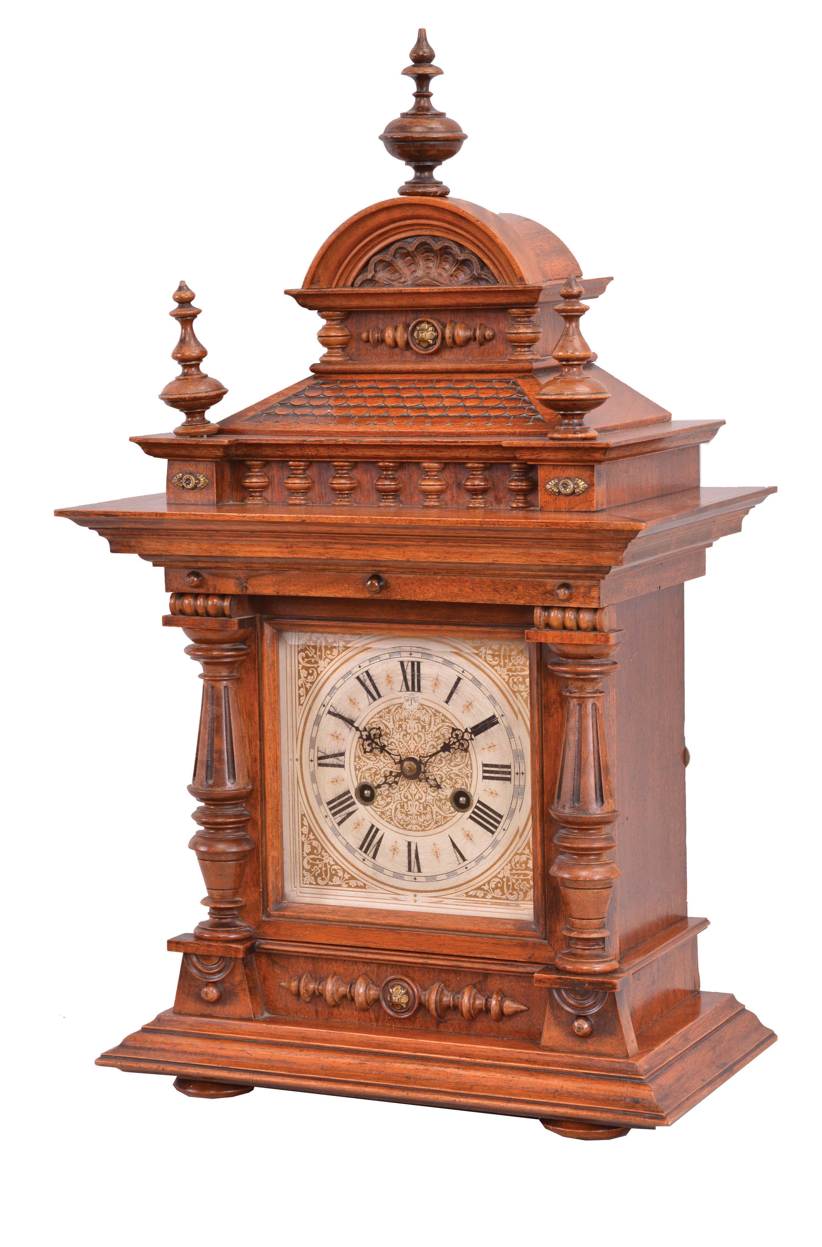 Gebrueder Junghans, Schramberg, Germany, mantel clock. 8 day, time and strike, spring driven movement in a walnut case with turned ornaments, polychrome paper dial, and blued steel hands. — Antique Clocks Price Guide