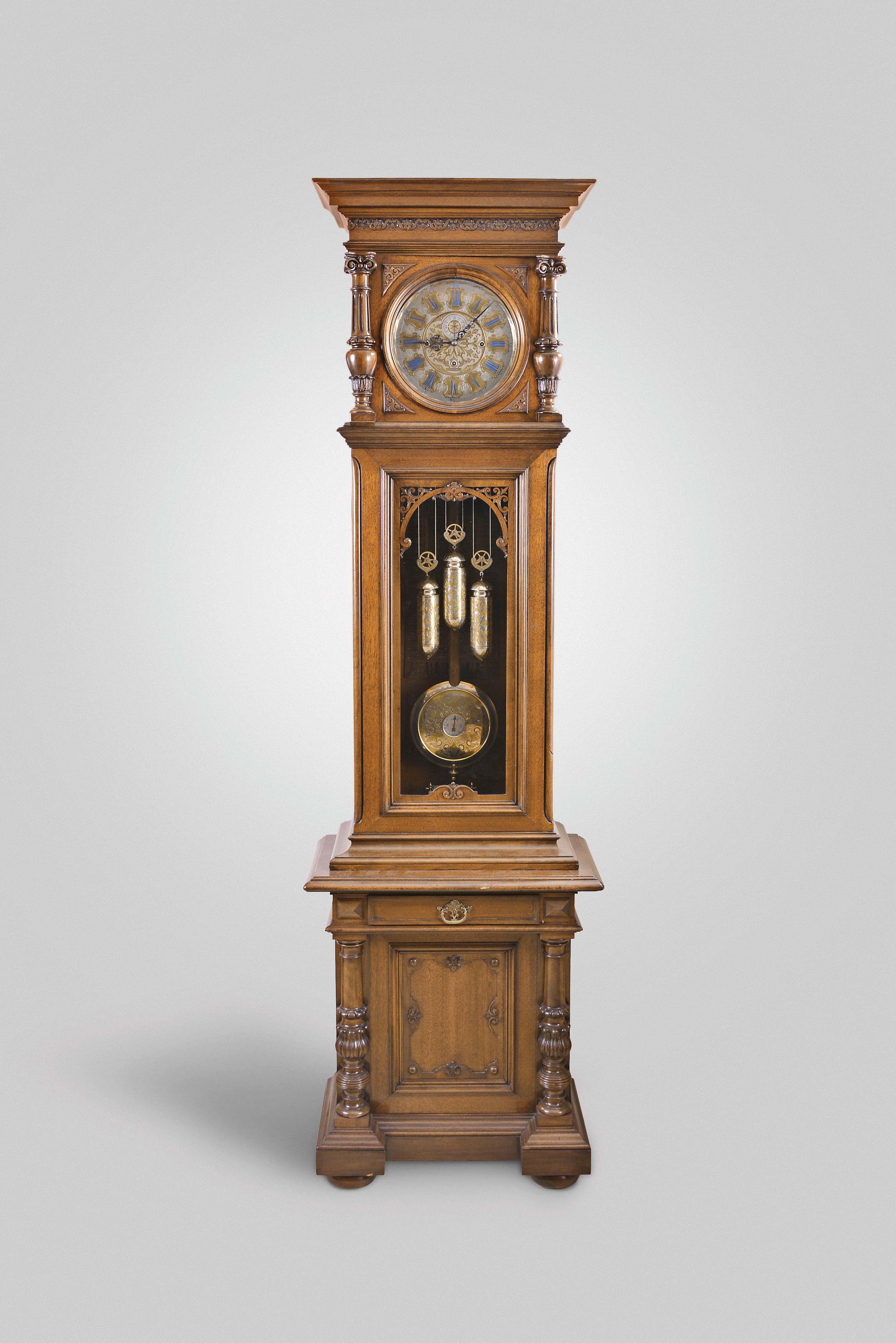 Anton Jezek, Wien, Austria, 30 day, time, strike &amp; grande sonnerie, weight driven movement in a two piece carved walnut case with carved and turned half columns flanking dial, carved fleur-de-lis style trim over trunk door glass over a base with a single drawer, cabinet and two carved and turned 3/4 columns resting on bun feet. The intricately engraved nickel plated dial has blue numerals on raised engraved brass plaques with maker's signature "Ant. Jezek" and matching pendulum disc and weights. — Antique Clocks Price Guide