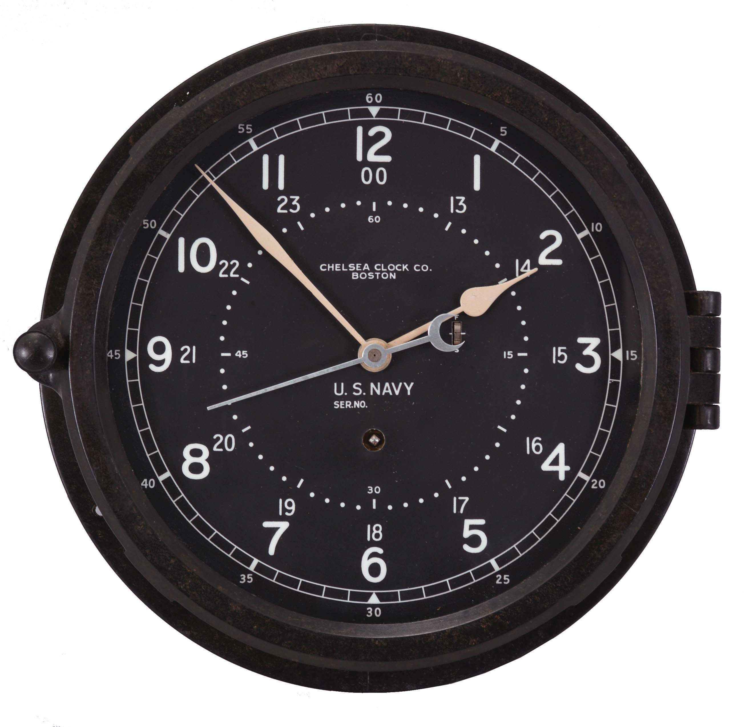 Chelsea Clock Co., Boston, Mass., "12E Deck &amp; Engine Room Clock", 8 day, time only, spring driven movement with jeweled lever escapement and center seconds in a black phenolic case with hinged bezel, 8.5 inch black dial signed by the maker and with "U.S. Navy", 12 and 24 hour markers, white spade hands, movement serial number 785464, c1974. — Antique Clocks Price Guide