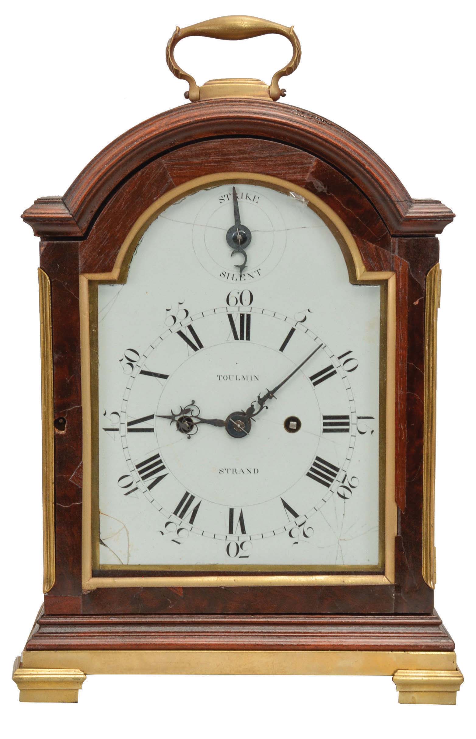 Samuel Toulmin, Strand, London, a Georgian mahogany bracket clock with enameled dial, the break arch case with polished brass furniture, and glazed sides, the case top and base molded on four sides, unusual white has Roman numerals, Arabic five minute markers, and strike/silent indicator in the arch, pierced, blued steel hands, two train fusee movement with verge escapement, the back plate engraved with acanthus, flowers, and C scrolls, and striking the hours on a bell. — Antique Clocks Price Guide