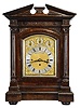 England, a monumental, quarter chiming table or bracket clock, the rosewood veneered and grain painted architectural case with molded base supporting a pair of columns with carved capitals below the carved entablature and broken pediment top, the sides with pierced, textile backed fret, composite dial with silvered roman numeral chapter ring, and subsidiary chime control and regulation at top, the dial also bearing an engraved plaque "The Association of Diamond Merchants, Jewellers, and Silversmiths, 6, Grand Hotel Buildings, Trafalgar Square, London", three train fusee movement chiming on eight bells or four gongs, and striking the hours on a larger, fifth gong