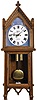 Louis Hoeber, 31 Duke St, Grosvenor Square, London, England, monumental Gothic revival wall clock, 8 day, time and strike, weight driven movement in an oak case with fleur-de-lis pediment top, and egg and dart molding flanked by pinwheel carved side elements over glazed door exposing large brass pendulum bob and beat scale. The reverse painted glass Gothic roman numeral dial with gilt lattice surround on a blue ground has maker's signature, address and Gothic hands