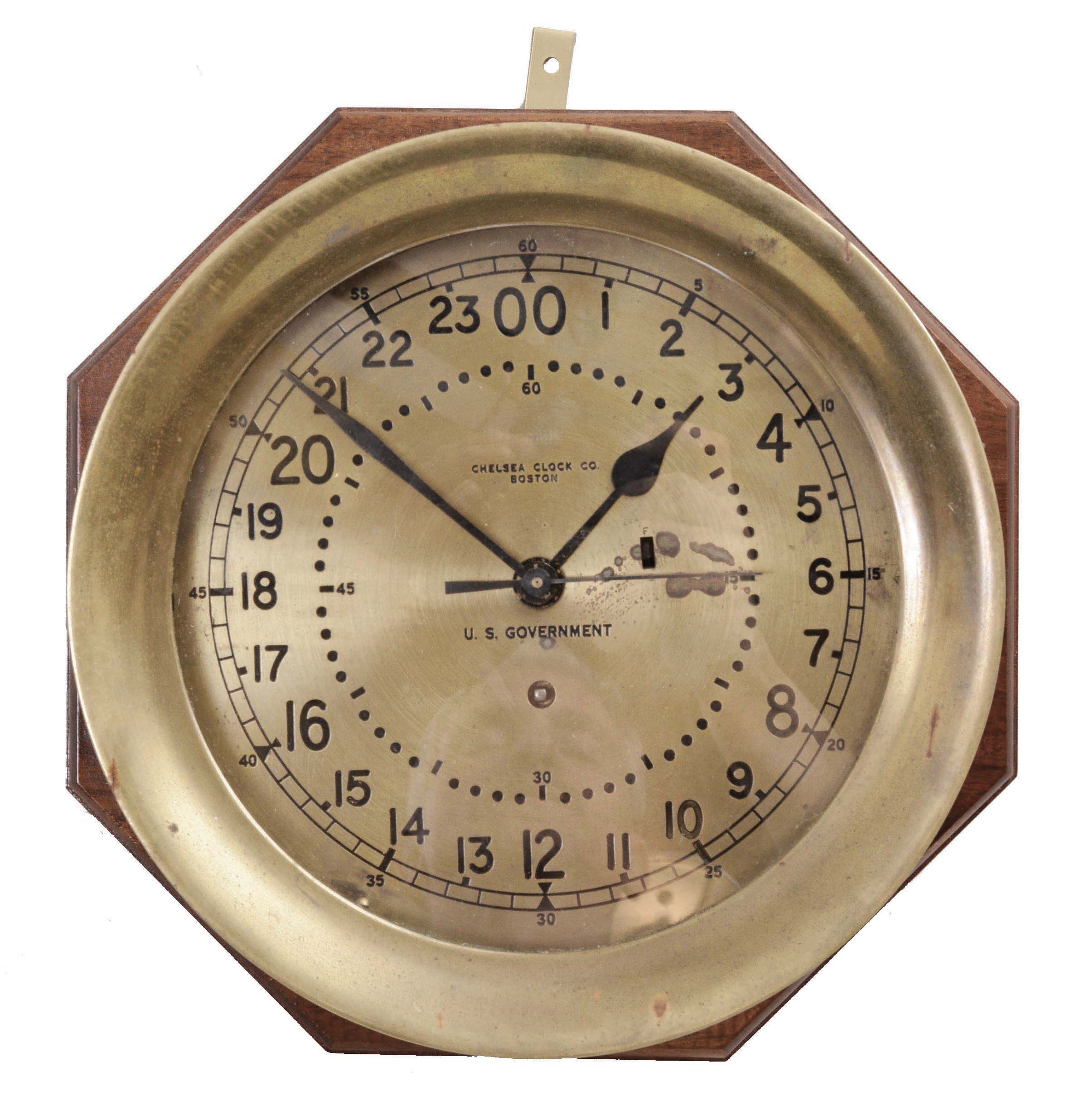 Chelsea Clock Co., Boston, Mass., "11E Deck and Engine Room" clock, 8 day, time only, spring-driven with jeweled movement, center seconds in a brass case with 8.5 inch dial showing 12/24 numerals, signed by Chelsea and "U.S. GOVERNMENT", all mounted to a mahogany backing board. — Antique Clocks Price Guide