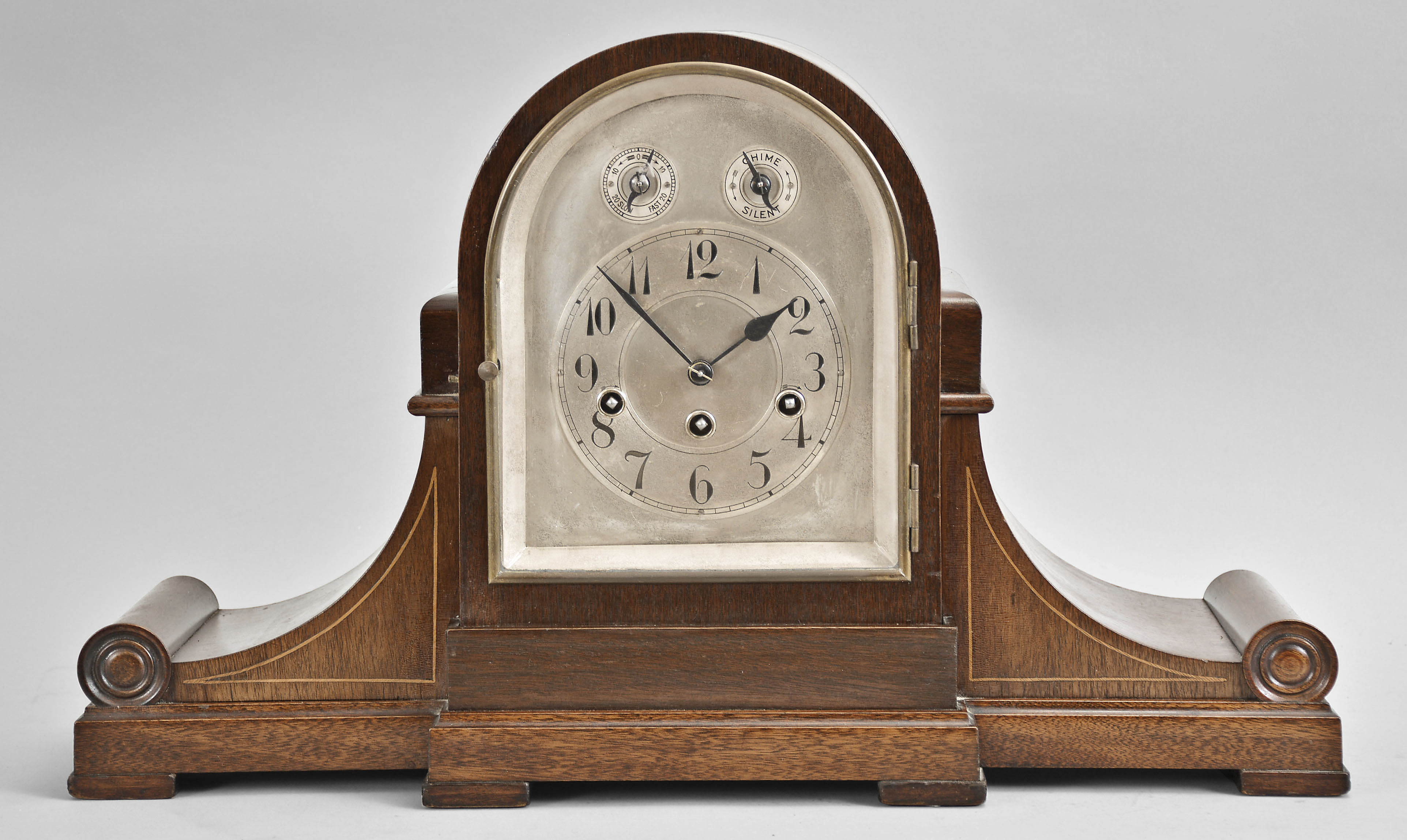 Gebruder Junghans, Schramberg, Germany, mantel clock, 8 day, time and strike with Westminster chime, spring driven movement in a tambour-form mahagony case with an arched silvered dial with Arabic numerals, subsidiary chime/silent selector and rate adjustment, all with with blued steel hands. — Antique Clocks Price Guide