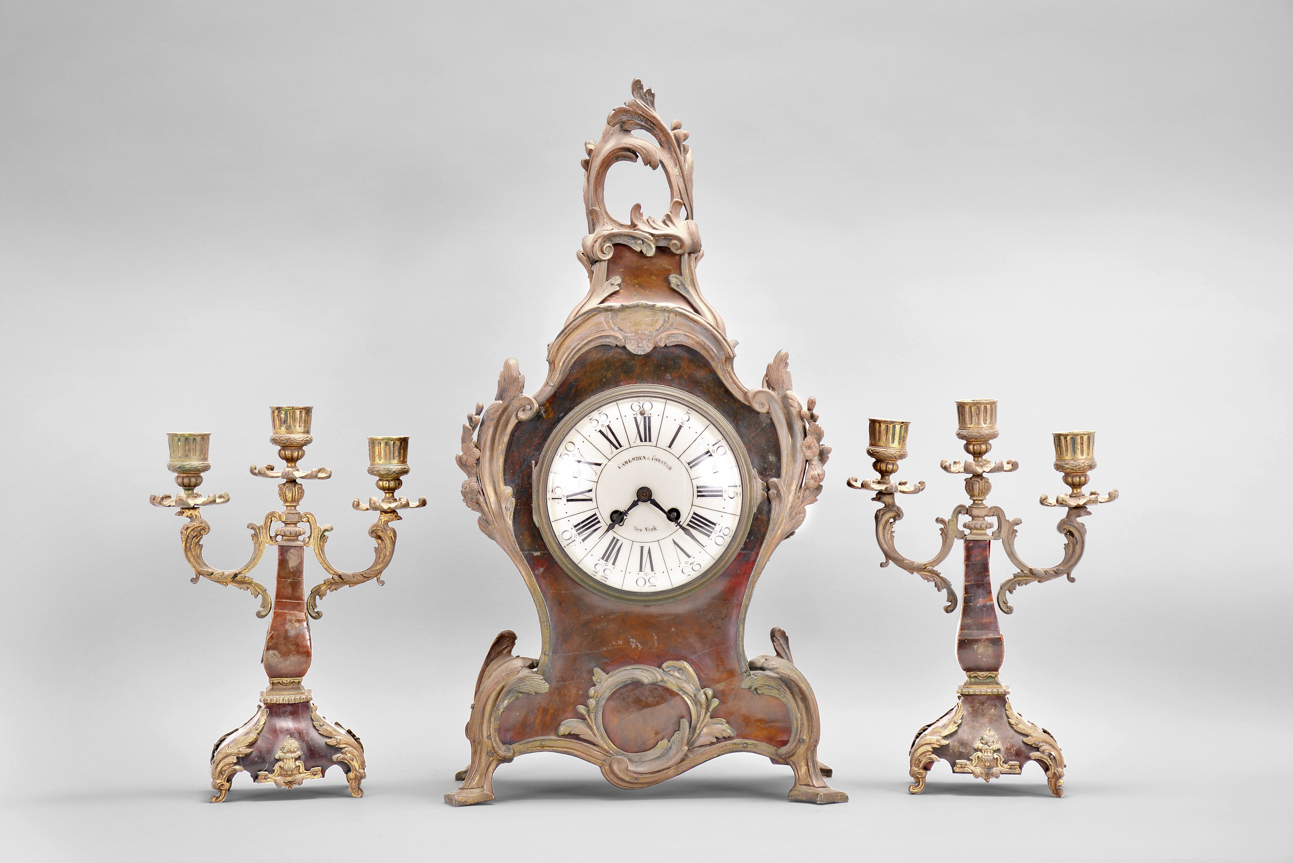 A.D. Mougin, Paris for Camerden &amp; Forster of New York, mantel clock, 8 day, time and strike, spring driven pendule de Paris movement in a Louis XV style case with tortoise shell veneer and rococo style brass ornament, white enamel dial with retailer's name, steel hands, two matching candelabra holding 3 candles each. — Antique Clocks Price Guide