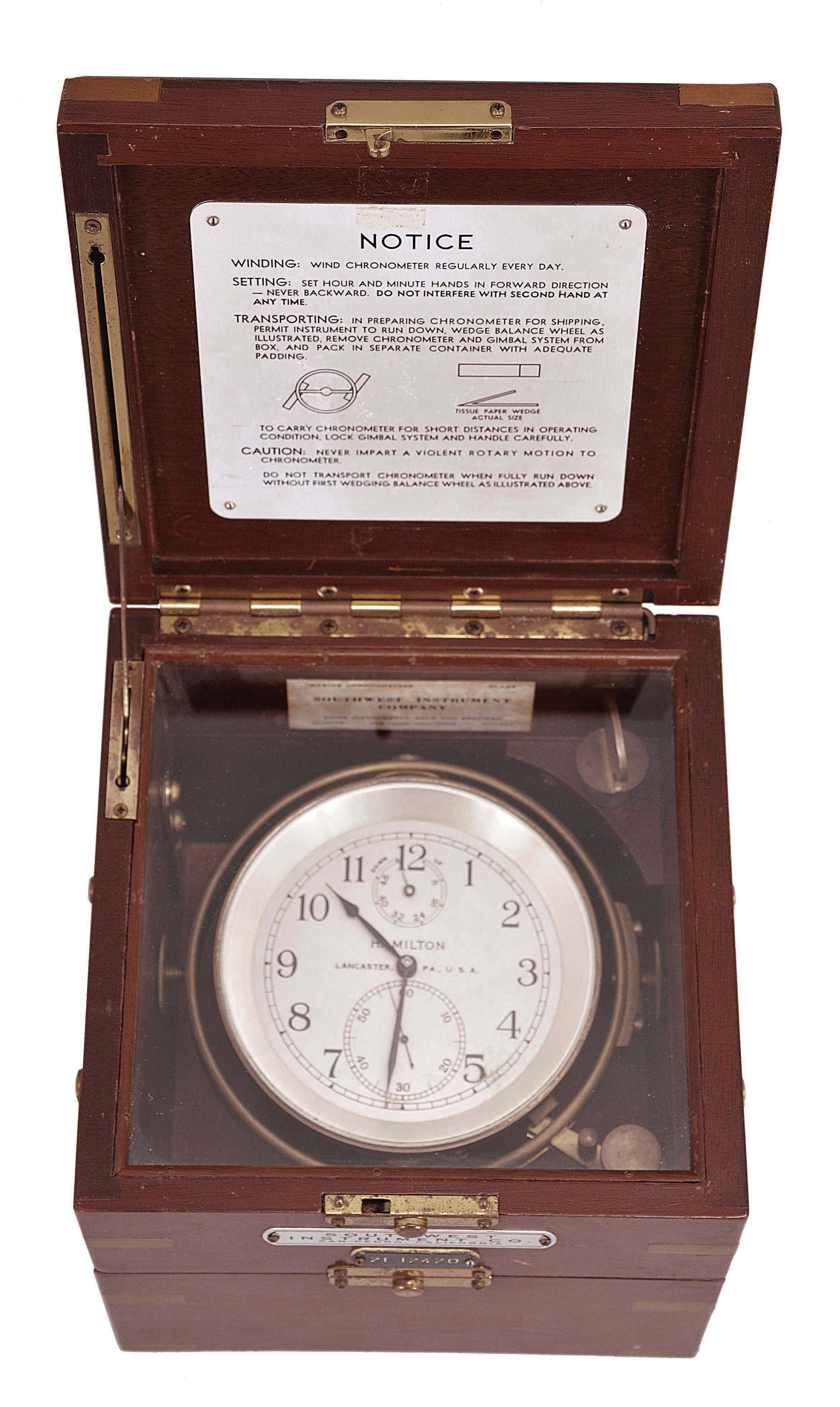 Hamilton Watch Co., Lancaster, Penn., model 21 marine Chronometer, 14 jewel, key wind and set fusee movement with grained nickel plates, spring detent escapement, large monometallic balance and helical balance spring, Arabic numeral metal dial with wind indicator, black painted steel spade and poker hands, with gimbaled brass bowl, contained in a three tier mahogany box with brass furniture and padded mahogany outer box with leather strap, serial #2E12420 — Antique Clocks Price Guide