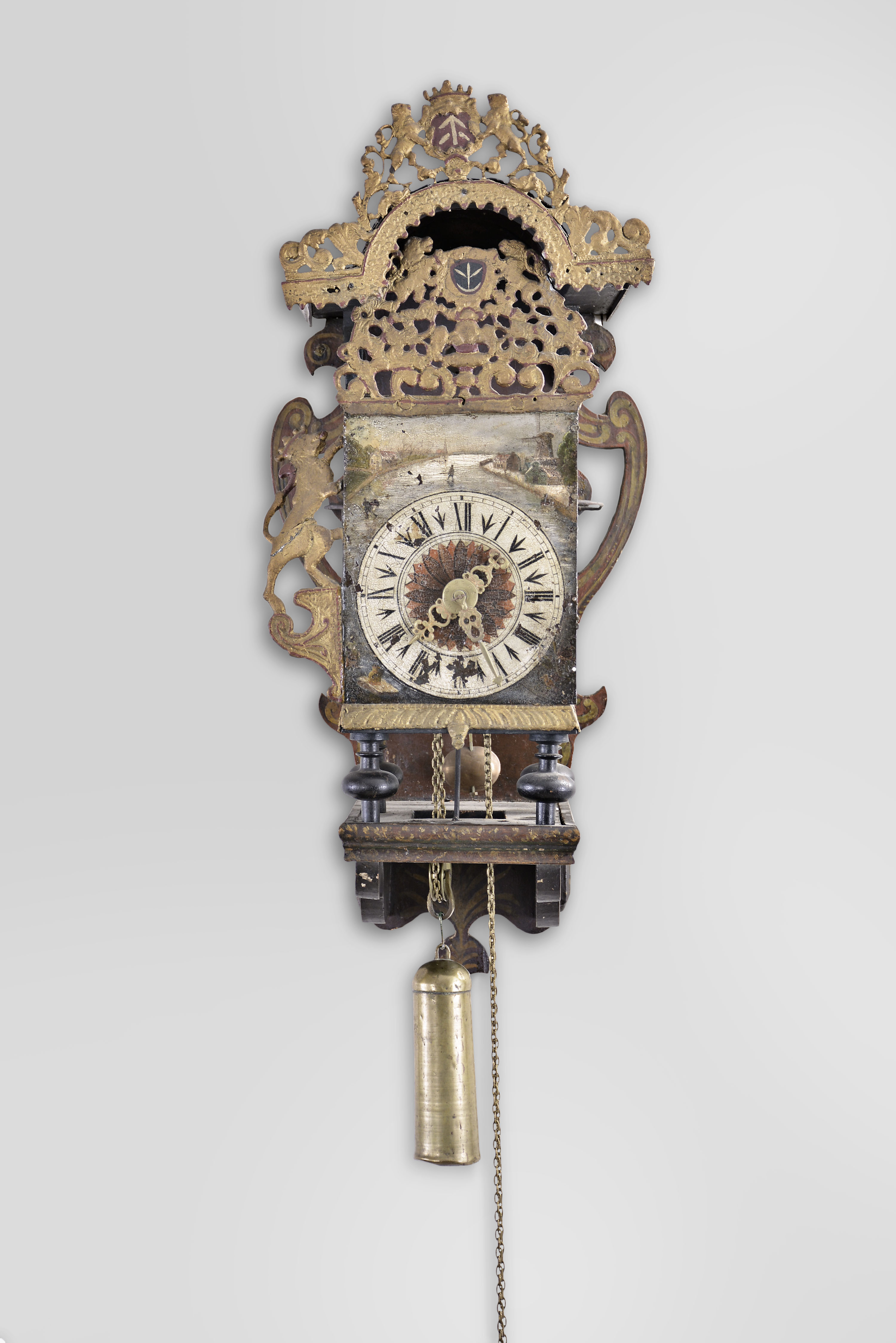 Netherlands, Frisian stoelklok, 30 hour, time and strike, weight driven movement with verge escapement, the clock resting on a polychrome painted shelf with scrolled decorations and lead ornaments with crowned lions, Roman numeral painted metal dial with landscape painting above, and pierced brass hands. — Antique Clocks Price Guide